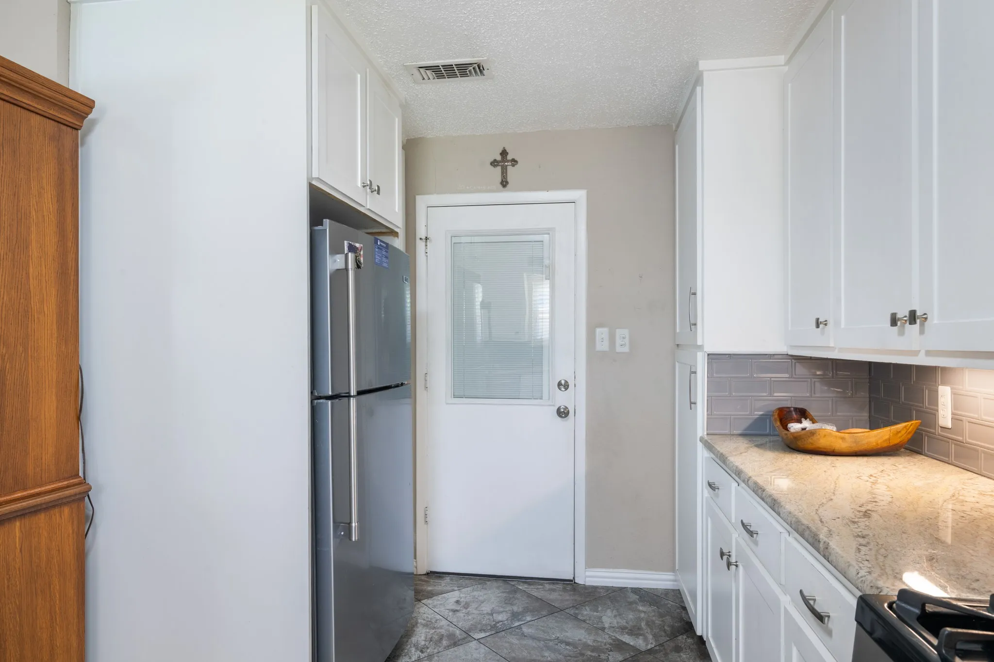 Updated kitchen featuring white cabinetry with hardware accents, stainless steel refrigerator, granite countertops, subway tile backsplash, and stainless steel range