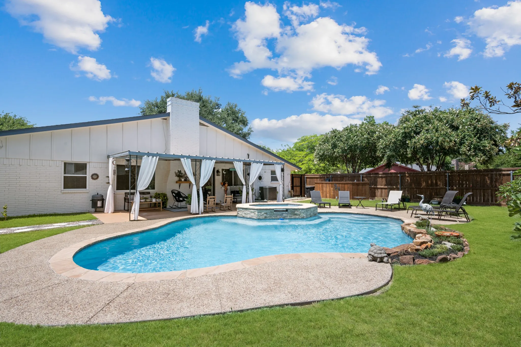 Expansive backyard featuring a large swimming pool with an integrated spa, stone coping, and a surrounding concrete patio