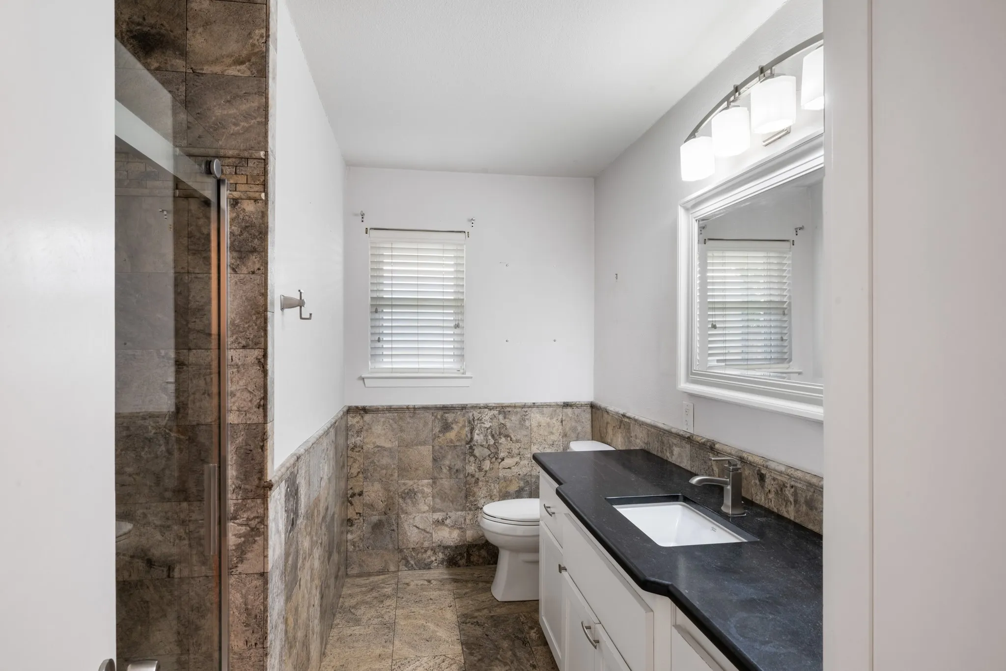Spa-inspired bathroom featuring dual vanity with black stone countertop and white cabinetry, ceramic tile flooring, and an oversized walk-in shower with mixed stone surround