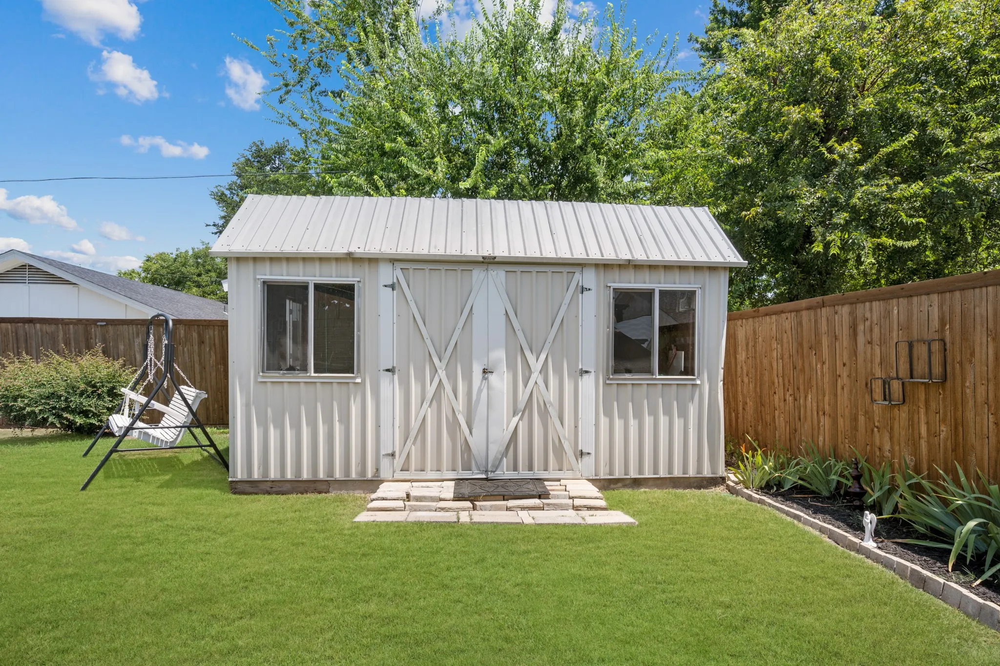 Charming backyard retreat featuring a classic board-and-batten storage shed with metal roof, dual barn-style doors, and paired windows
