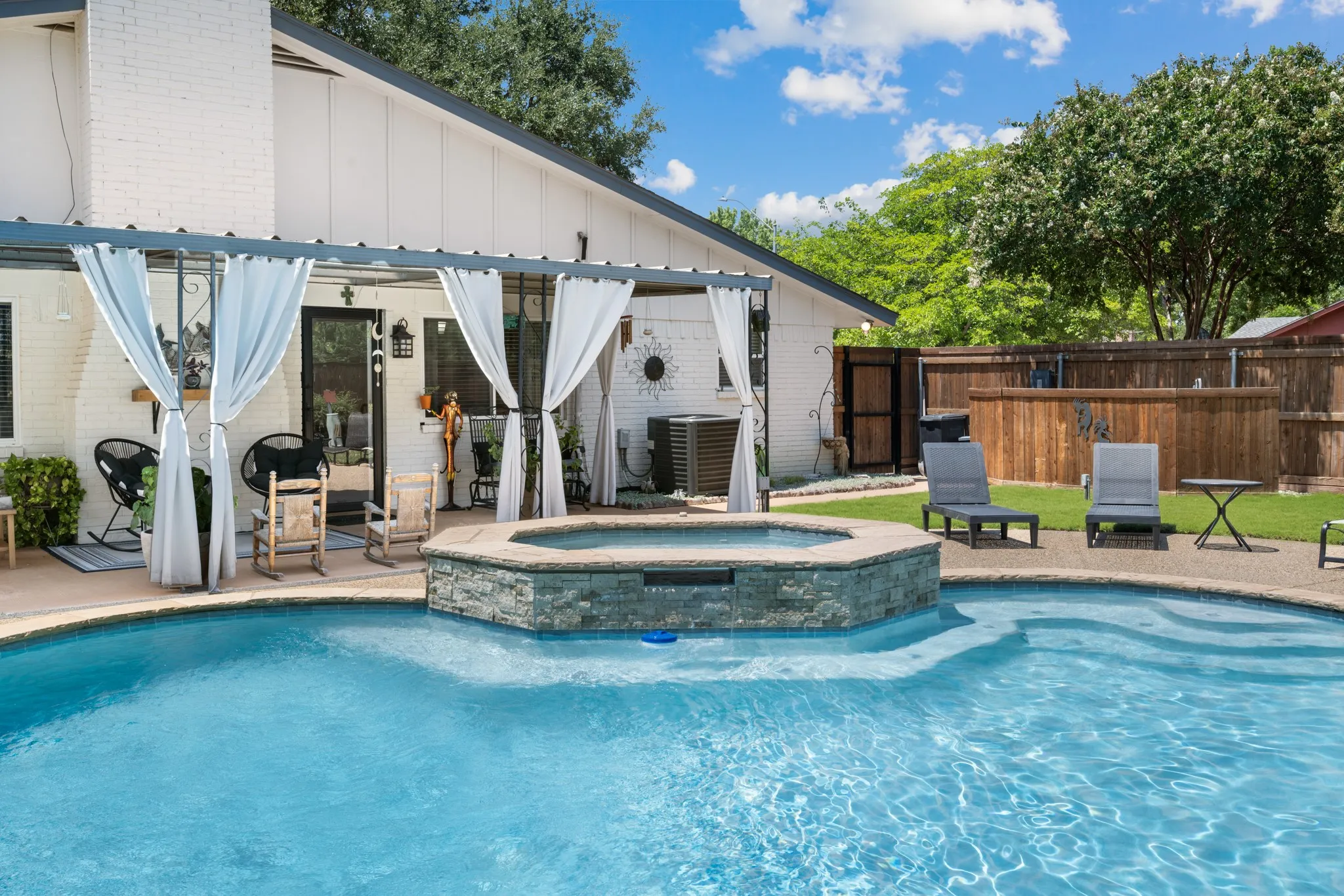 Backyard featuring a built-in swimming pool with an integrated spa, a stone-clad spa surround, and a paved patio area