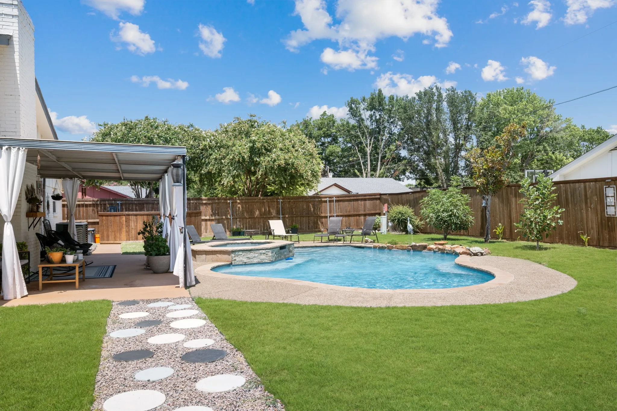 Expansive backyard oasis featuring a resort-style in-ground swimming pool with curved design, surrounding concrete decking, and manicured lawn