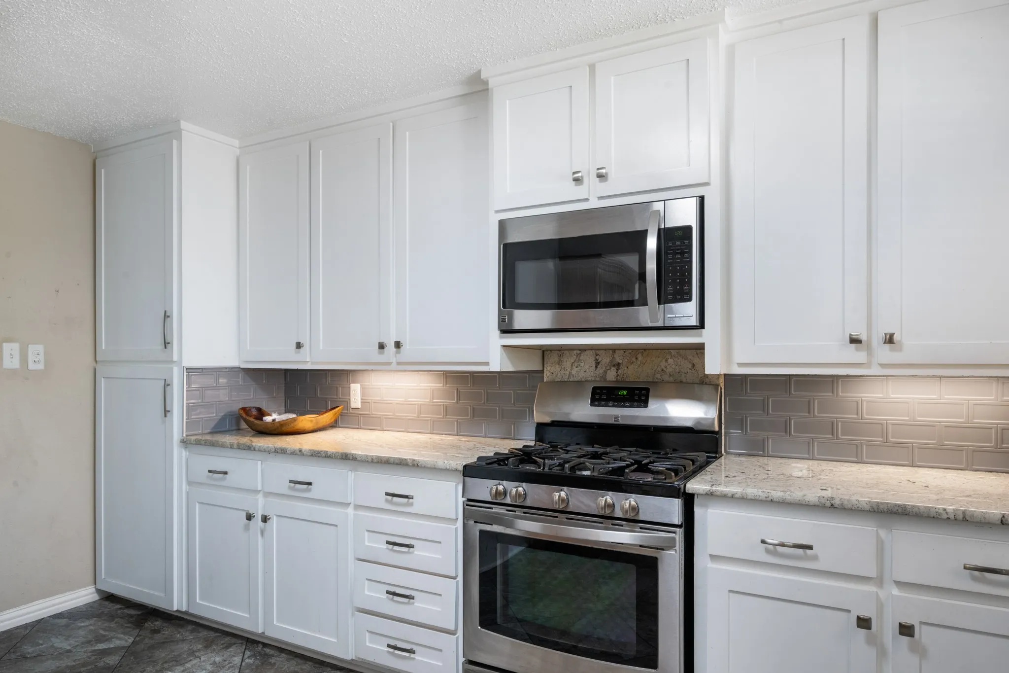 Modern kitchen featuring crisp white shaker-style cabinetry with brushed nickel hardware, stainless steel gas range with dual ovens, and built-in microwave