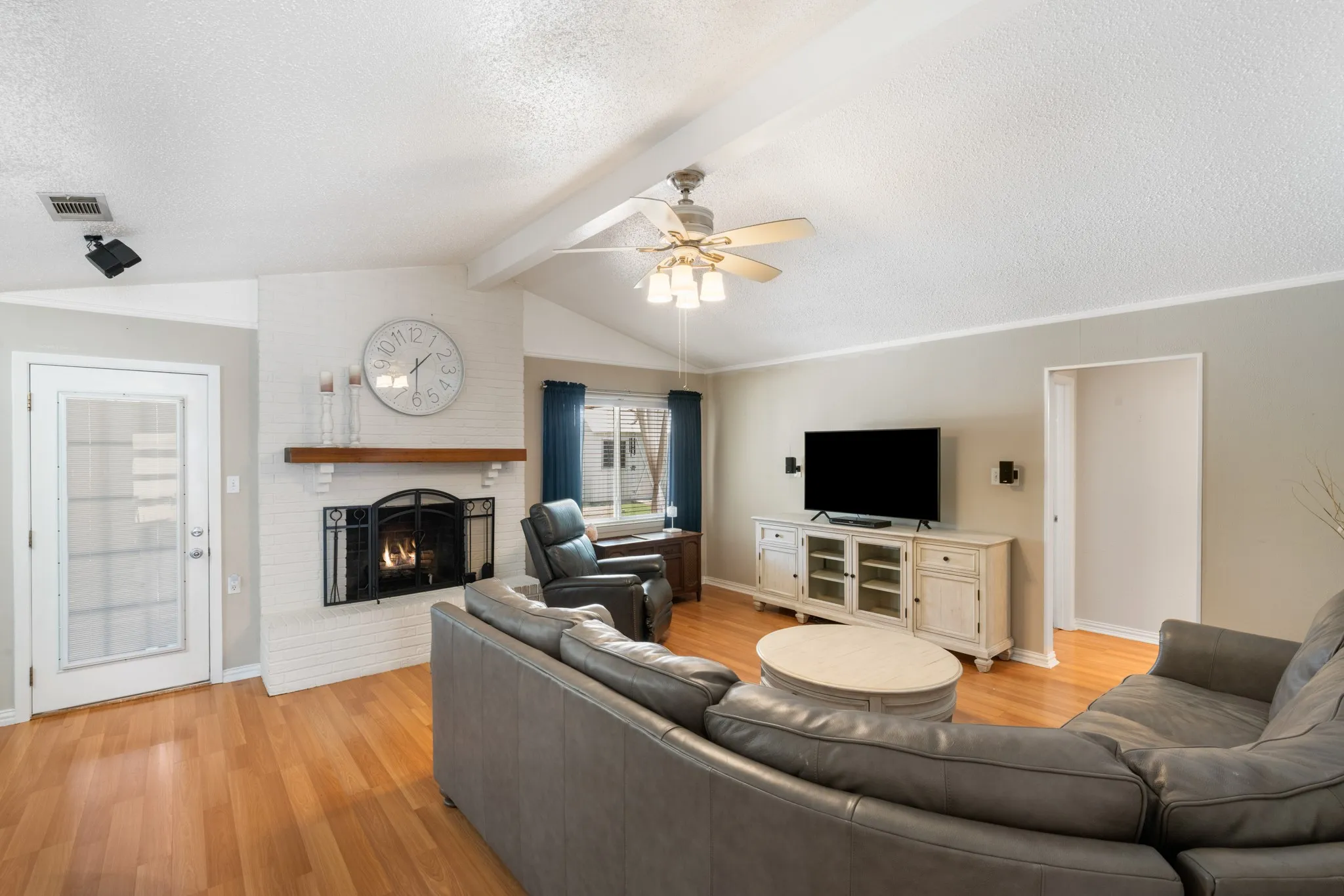 Spacious living room featuring a curved sectional arrangement, wood-finish flooring, and a ceiling fan with integrated lighting