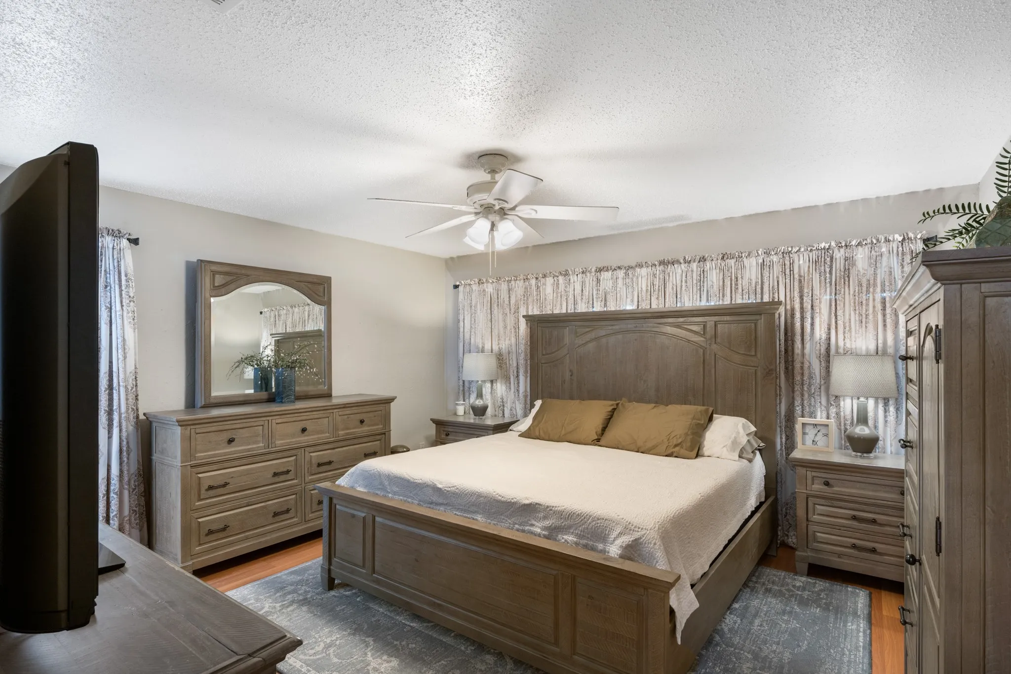 Spacious primary bedroom showcasing a wood-frame bed with upholstered headboard, coordinating wood-finish dresser with mirror, and matching nightstands