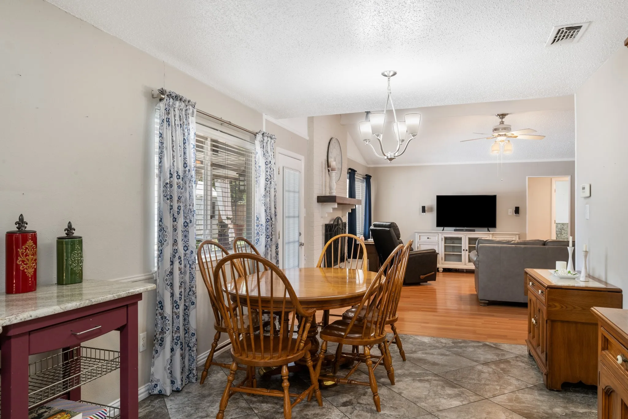 Open dining area with wood-finish flooring, a round pedestal dining table with Windsor-style chairs, and large windows dressed in patterned curtains