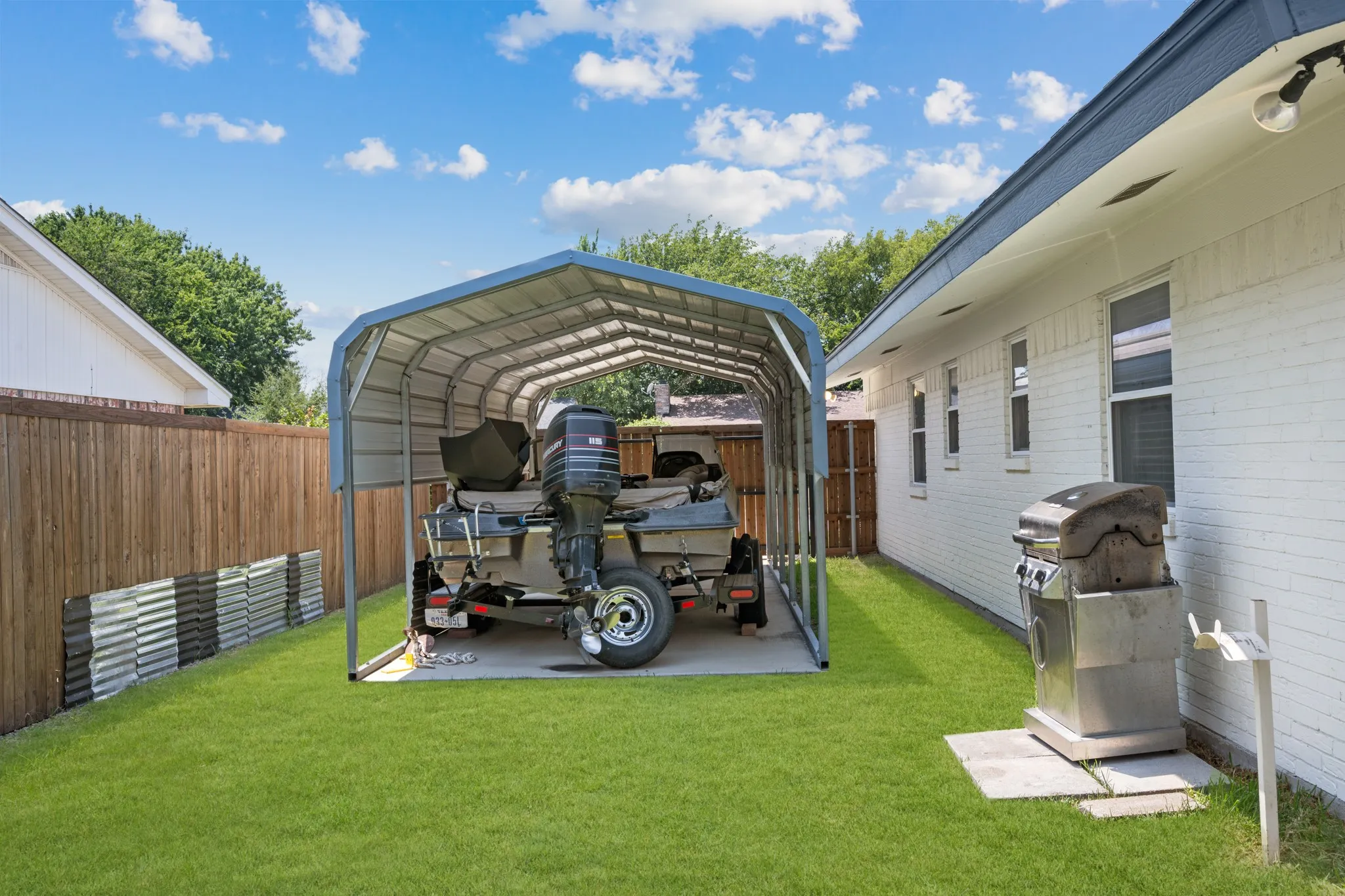 Spacious backyard oasis featuring a manicured lawn, mature landscaping, and a sturdy metal carport structure with arched roof design