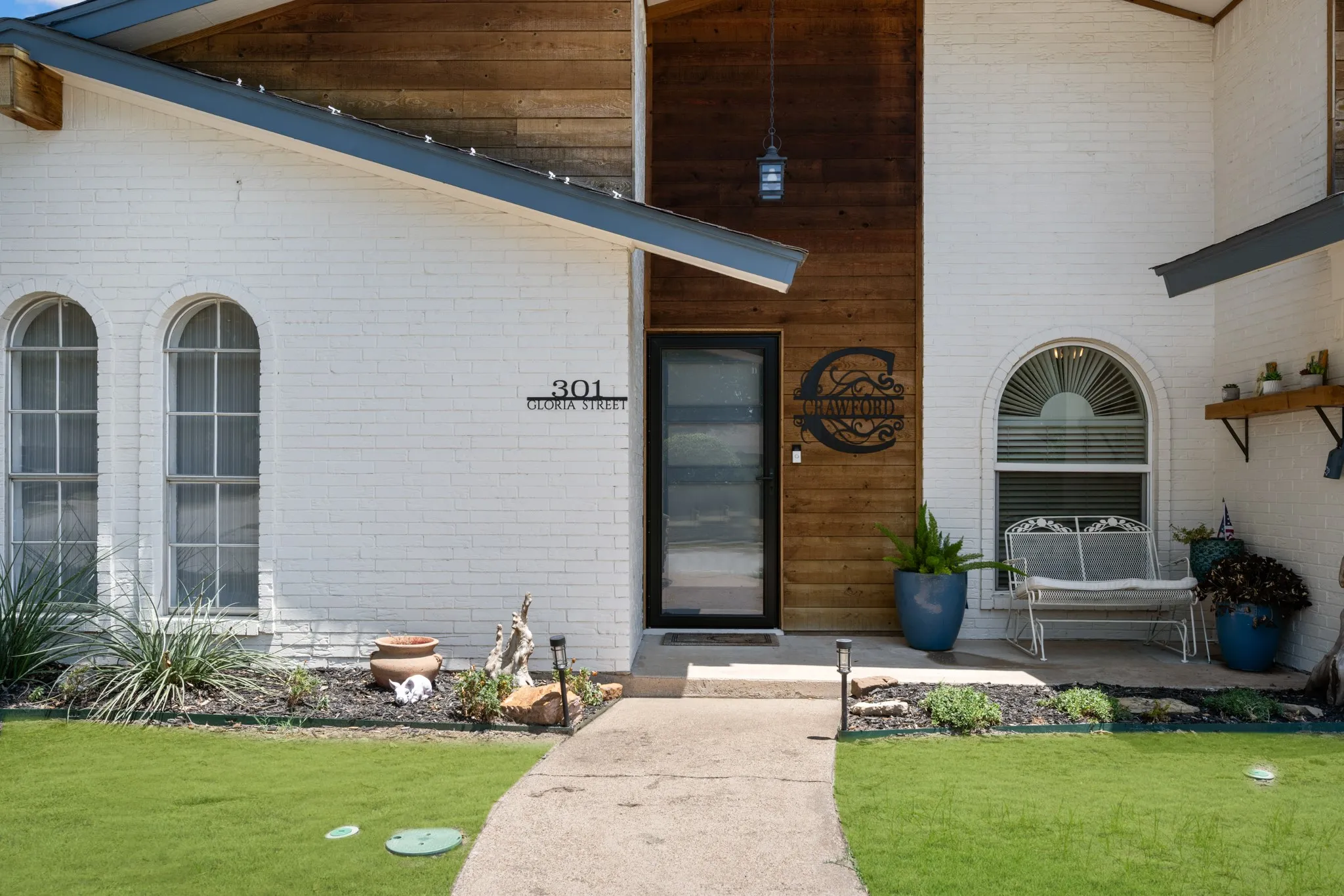 White brick exterior featuring a wood-paneled entry, arched windows, and a paved walkway