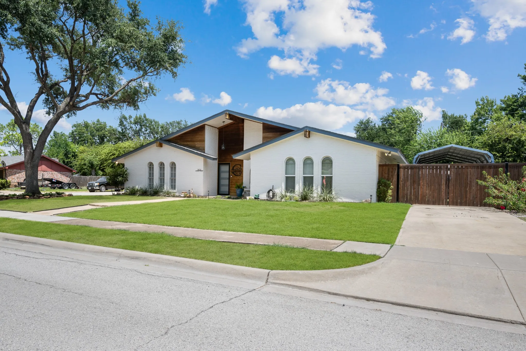 White brick exterior with a wood-clad entry, featuring a concrete driveway, a wood fence, and a mature tree