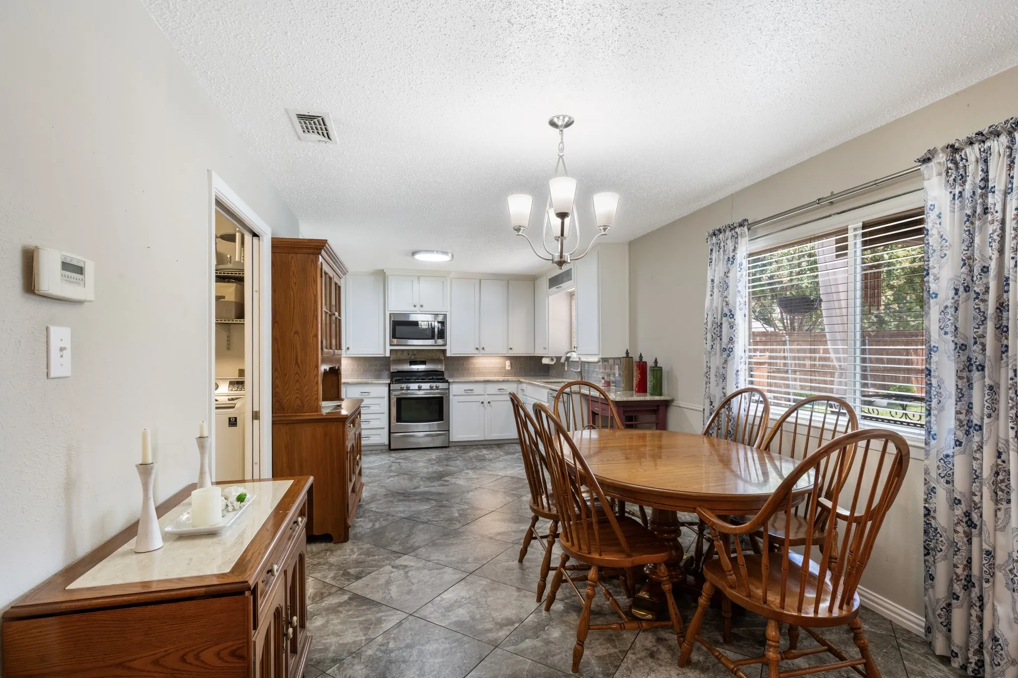 Kitchen and dining area featuring white cabinetry, stainless steel appliances, tile flooring, and a chandelier