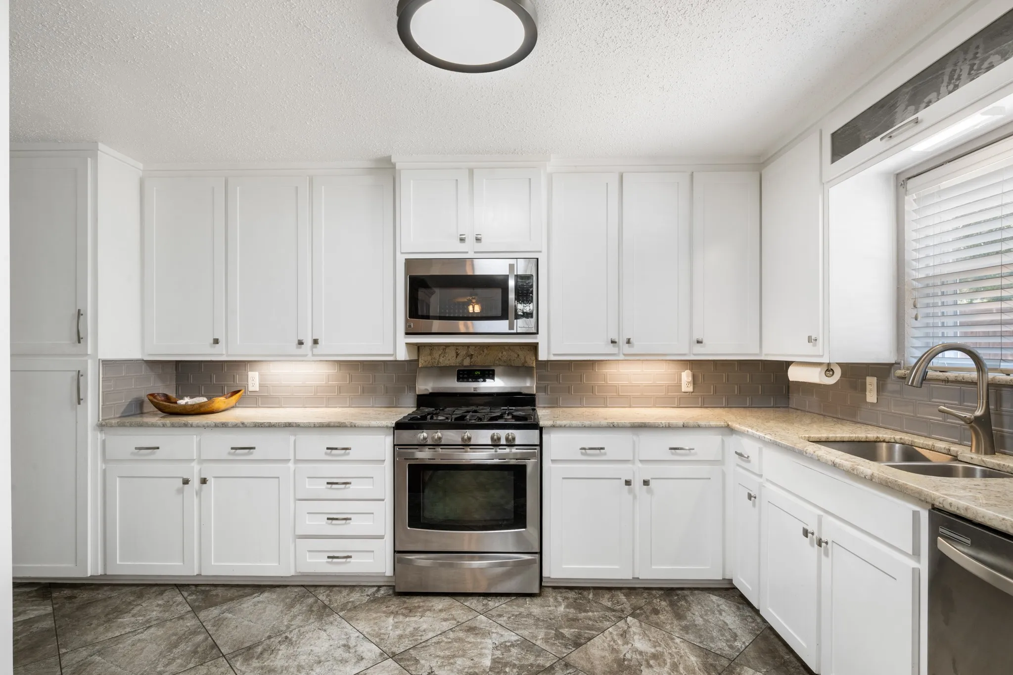 Bright and spacious kitchen featuring crisp white cabinetry with brushed nickel hardware, stainless steel gas range and built-in microwave, quartz countertops, tile backsplash, and stainless steel sink with pull-down faucet