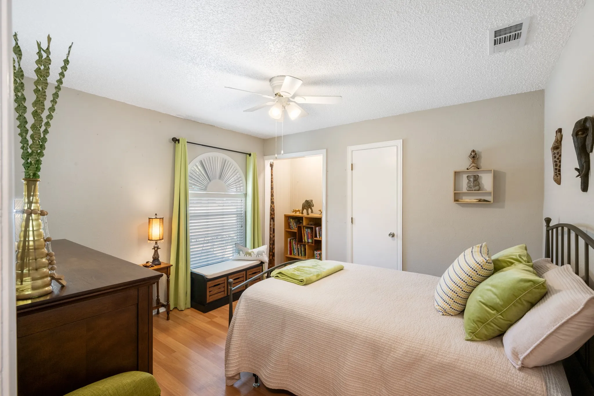 Bright bedroom featuring hardwood flooring, ceiling fan with integrated lighting, and large window with plantation shutters and natural light