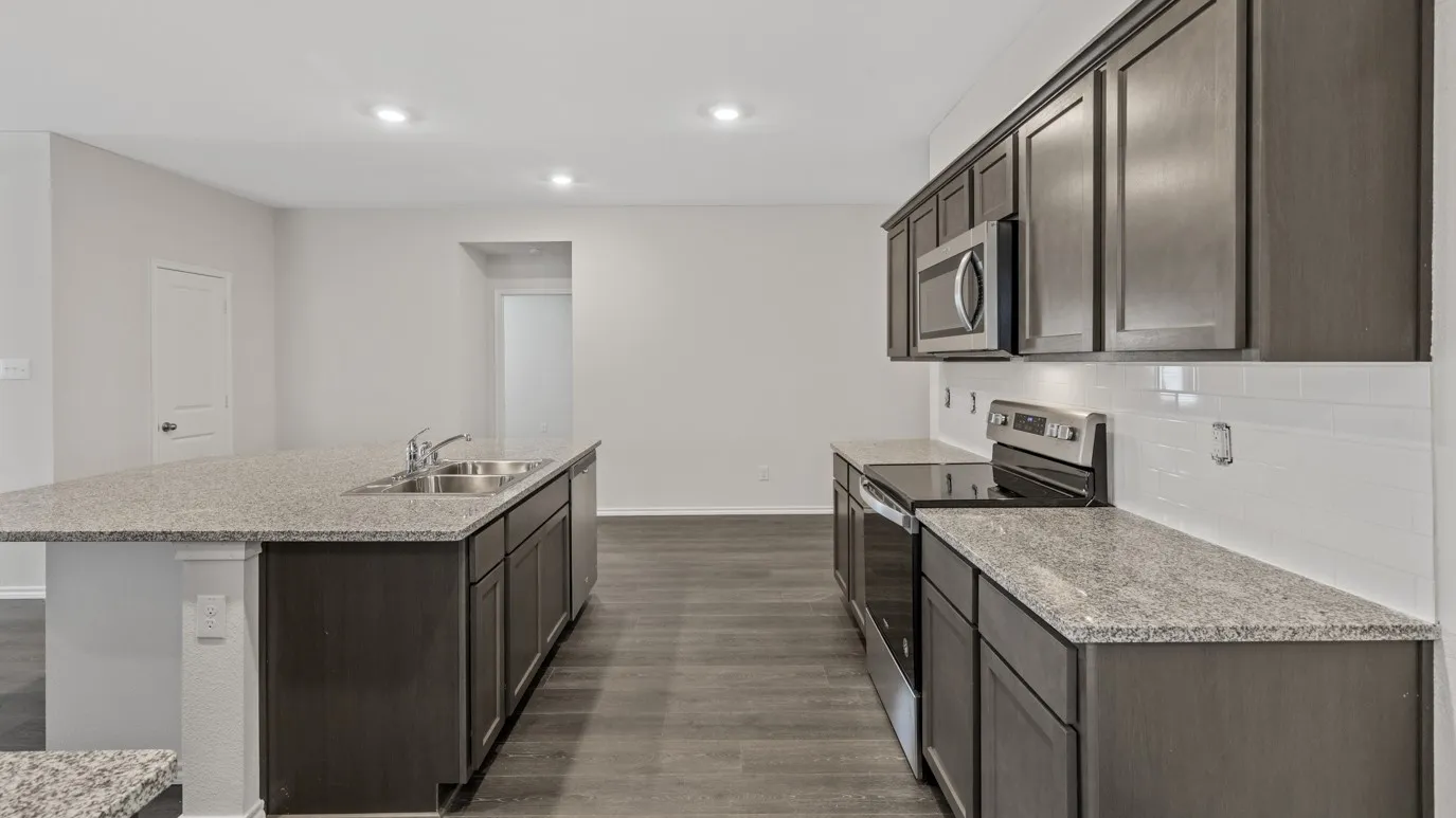 Kitchen featuring dark wood-finish cabinetry, light speckled countertops, stainless steel appliances, and a subway tile backsplash