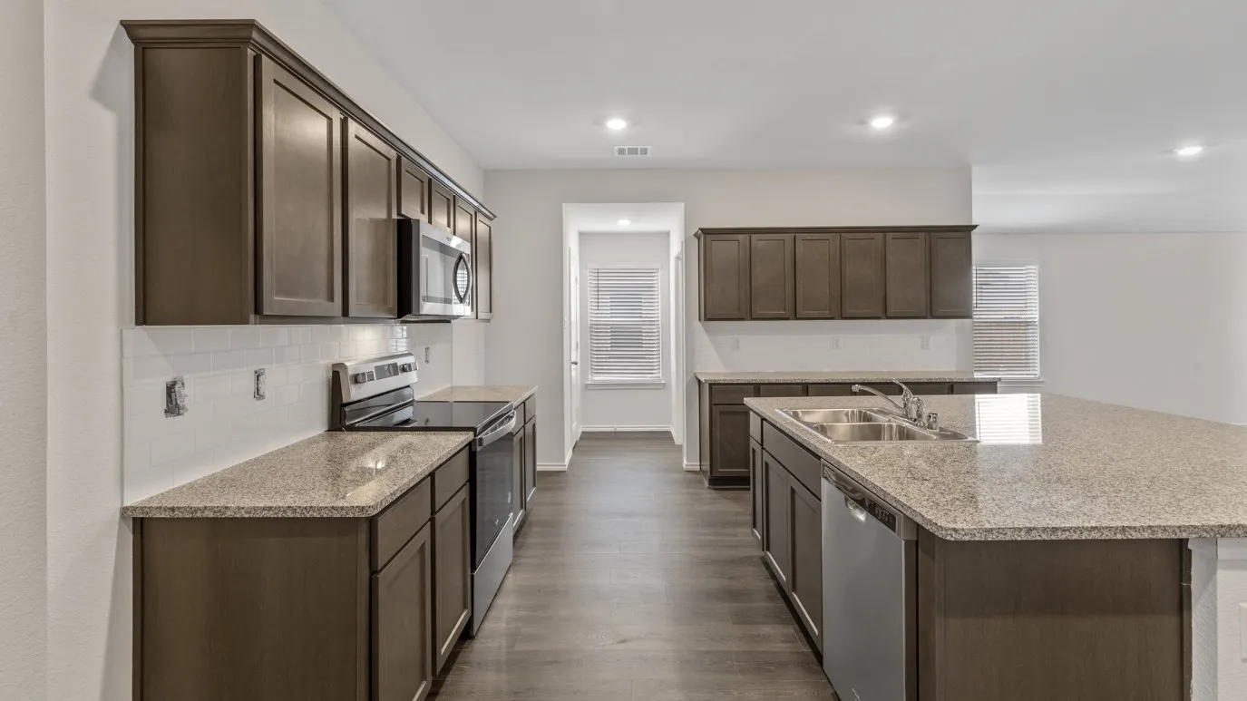 Open-concept kitchen featuring dark wood cabinetry, granite countertops, and stainless steel appliances, including a range, microwave, and dishwasher