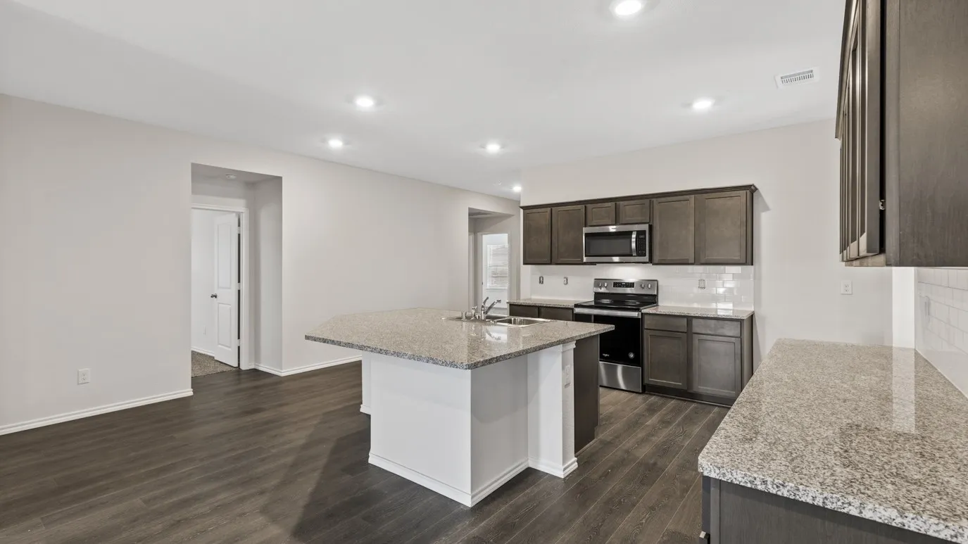 Open-concept kitchen featuring dark wood cabinetry, stainless steel appliances, granite countertops, and a white subway tile backsplash