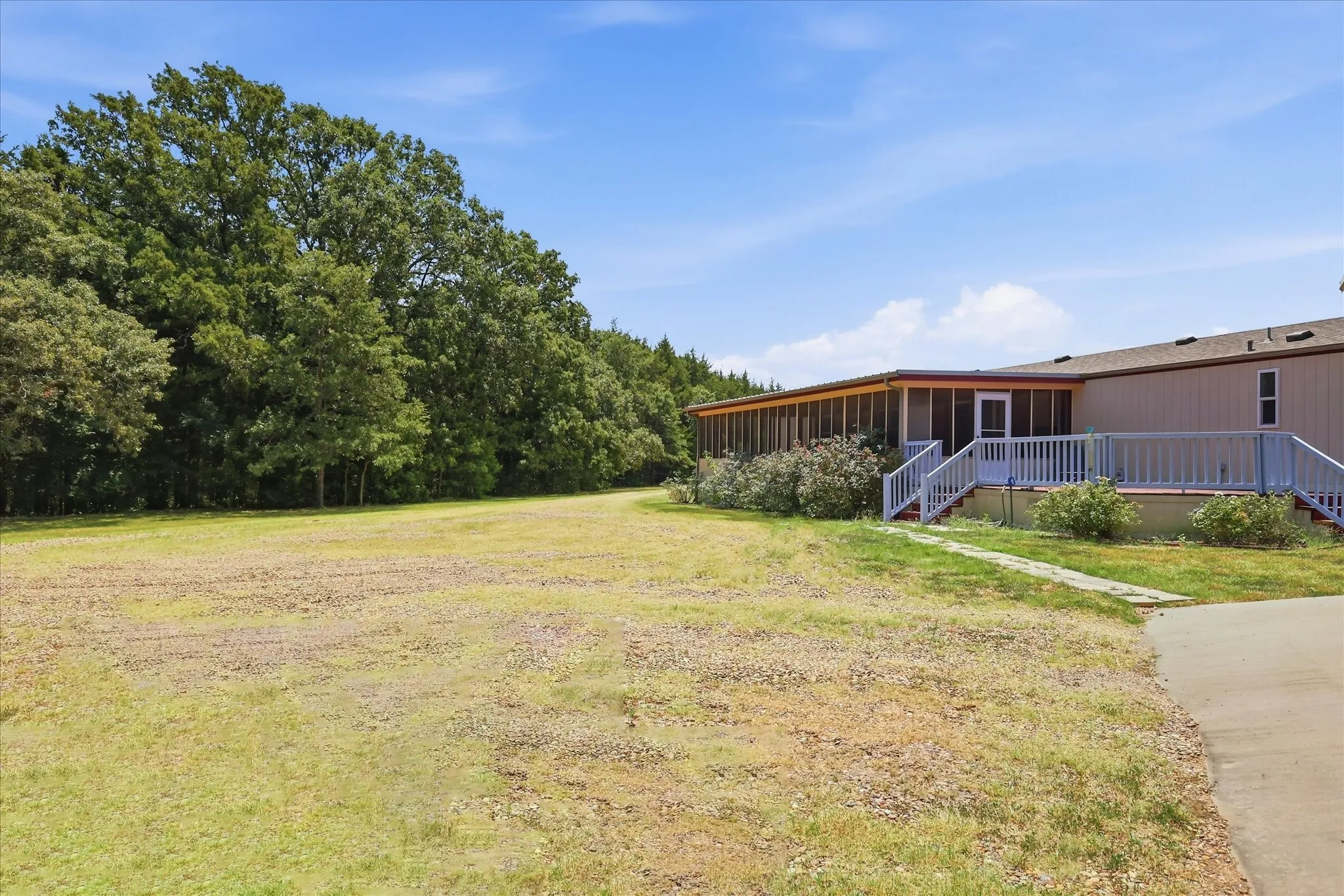 Property exterior featuring a screened porch, an open deck with white railings, and a concrete pathway leading to a paved area