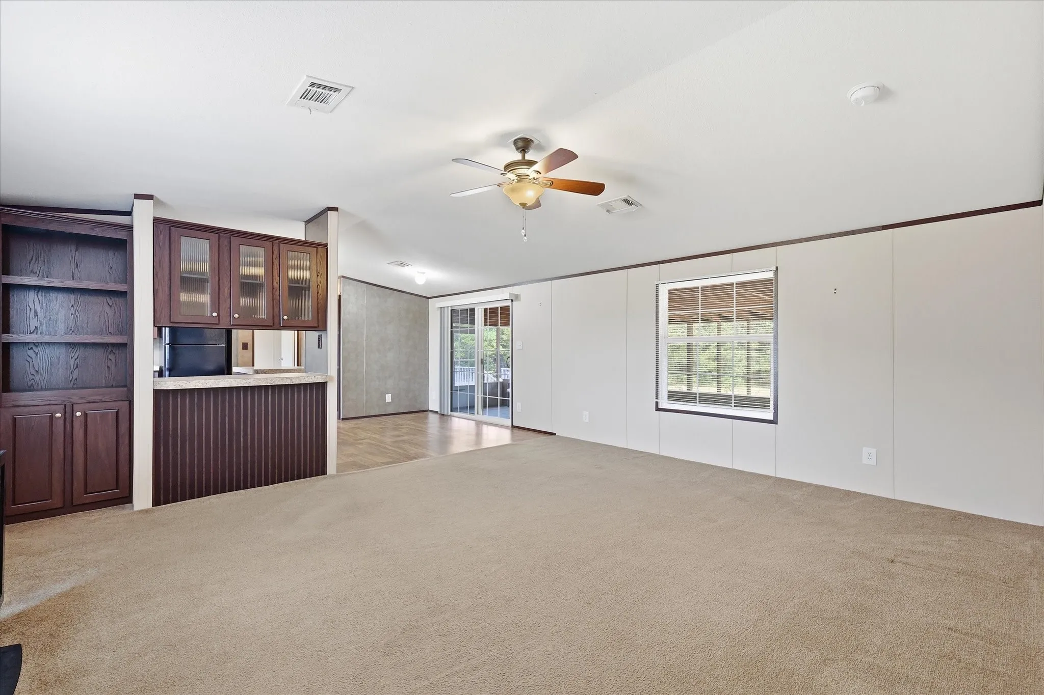Expansive carpeted living area featuring a built-in bookcase, a beverage bar with upper glass-front cabinets, and a ceiling fan