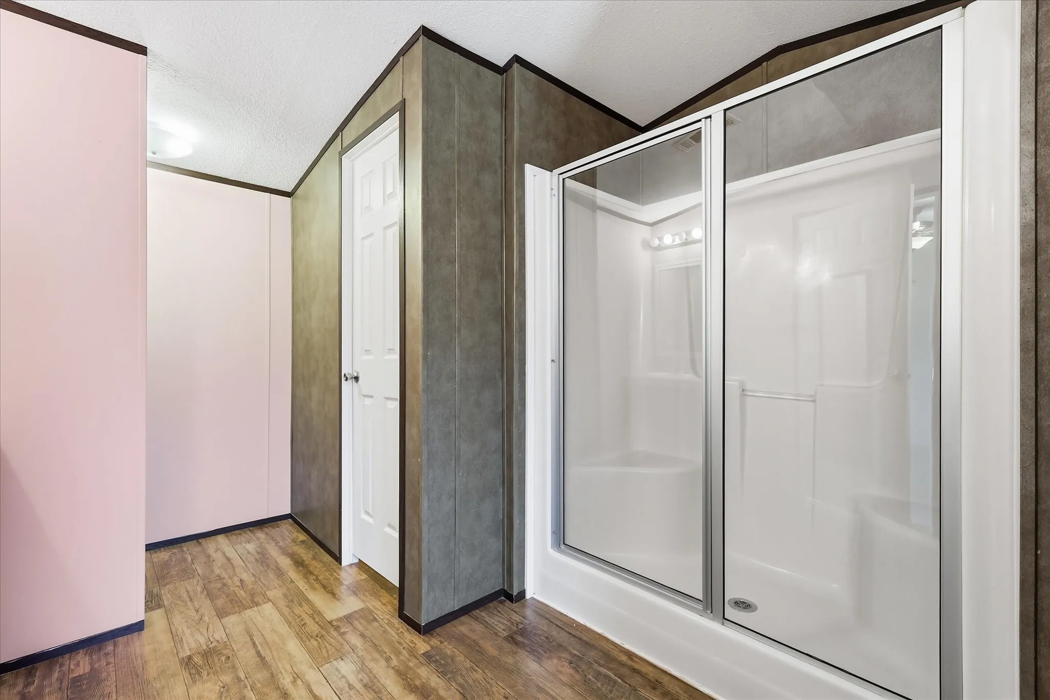 Primary Bathroom Suite featuring a frameless glass-enclosed shower with chrome hardware, wood-finish flooring, and neutral tile accents