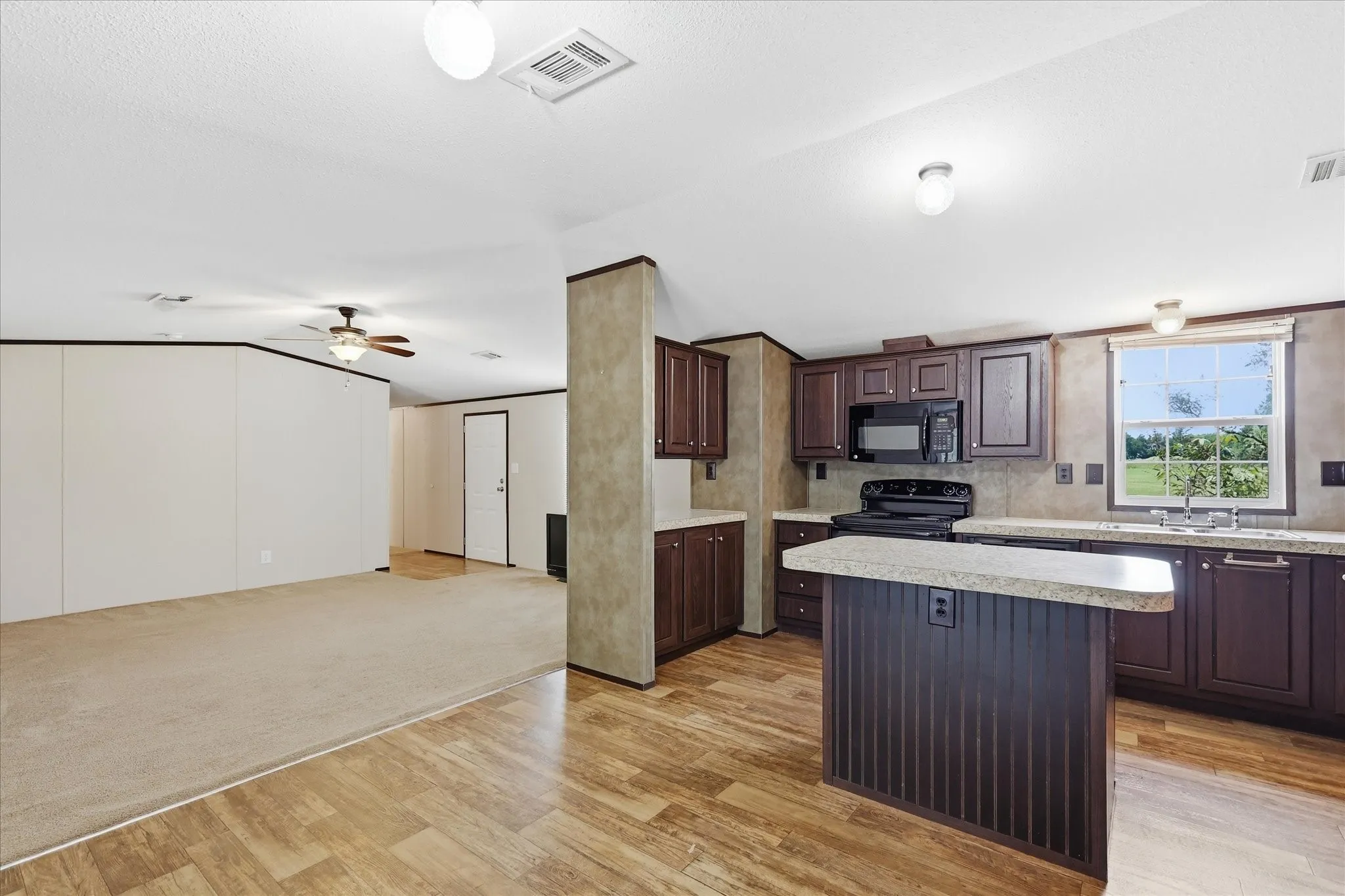 Well-appointed kitchen featuring dark wood cabinetry, a central island with a beadboard base, light-colored countertops, and modern black appliances