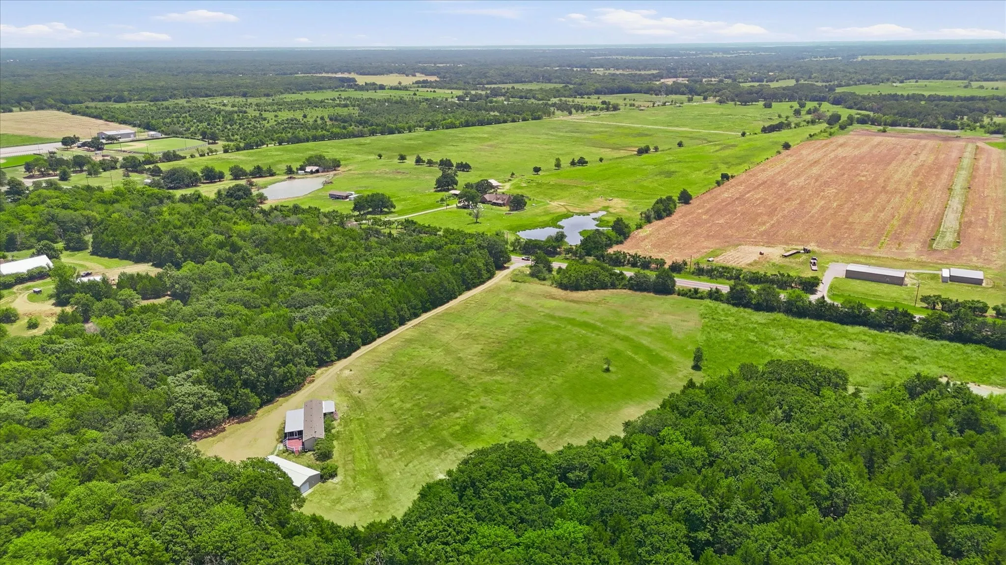 Expansive aerial showcasing a diverse landscape with wooded areas, open pastures, and cultivated fields