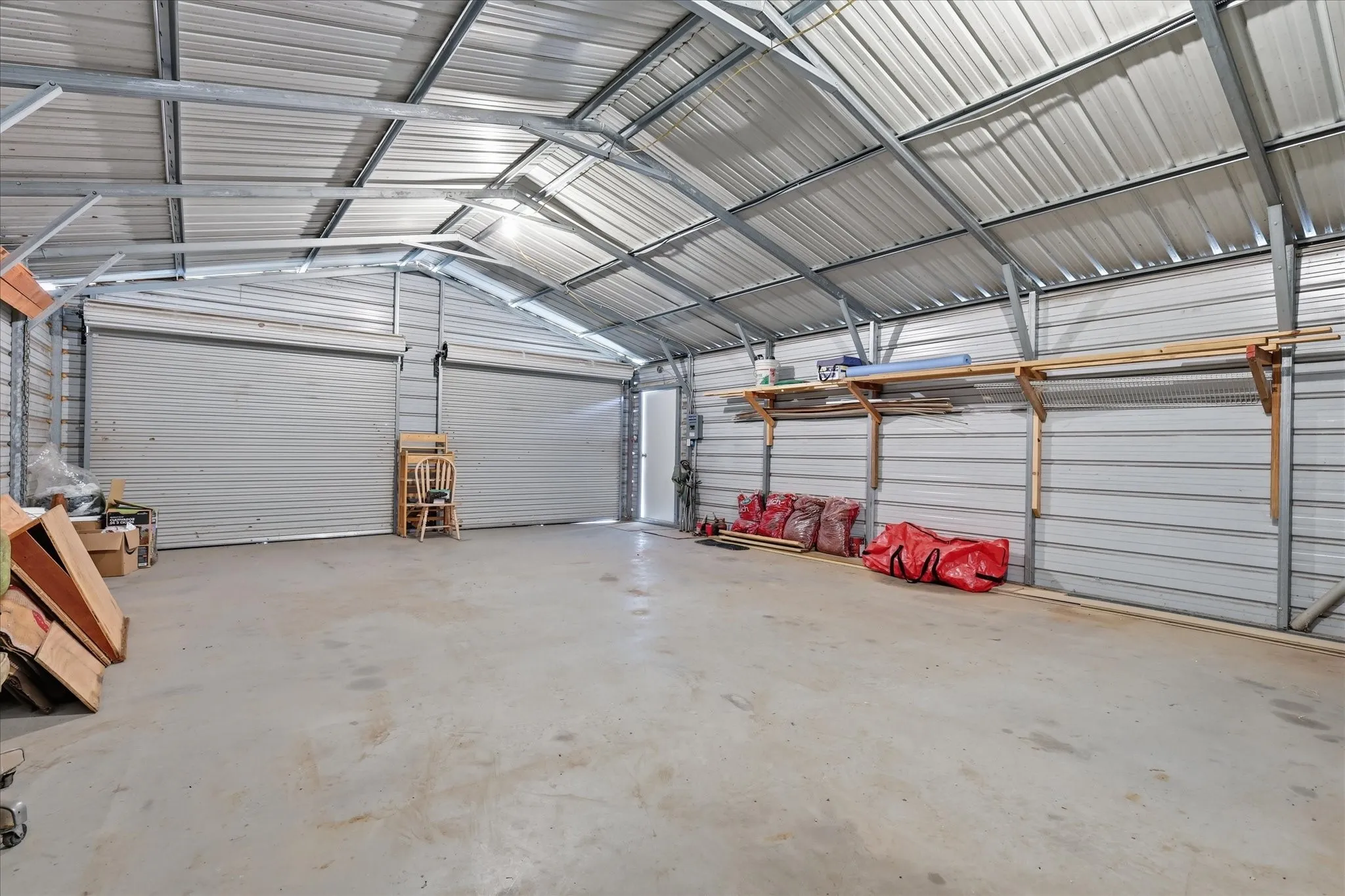 Metal structure featuring a concrete floor, two roll-up doors, an additional entry door, and exposed metal framing