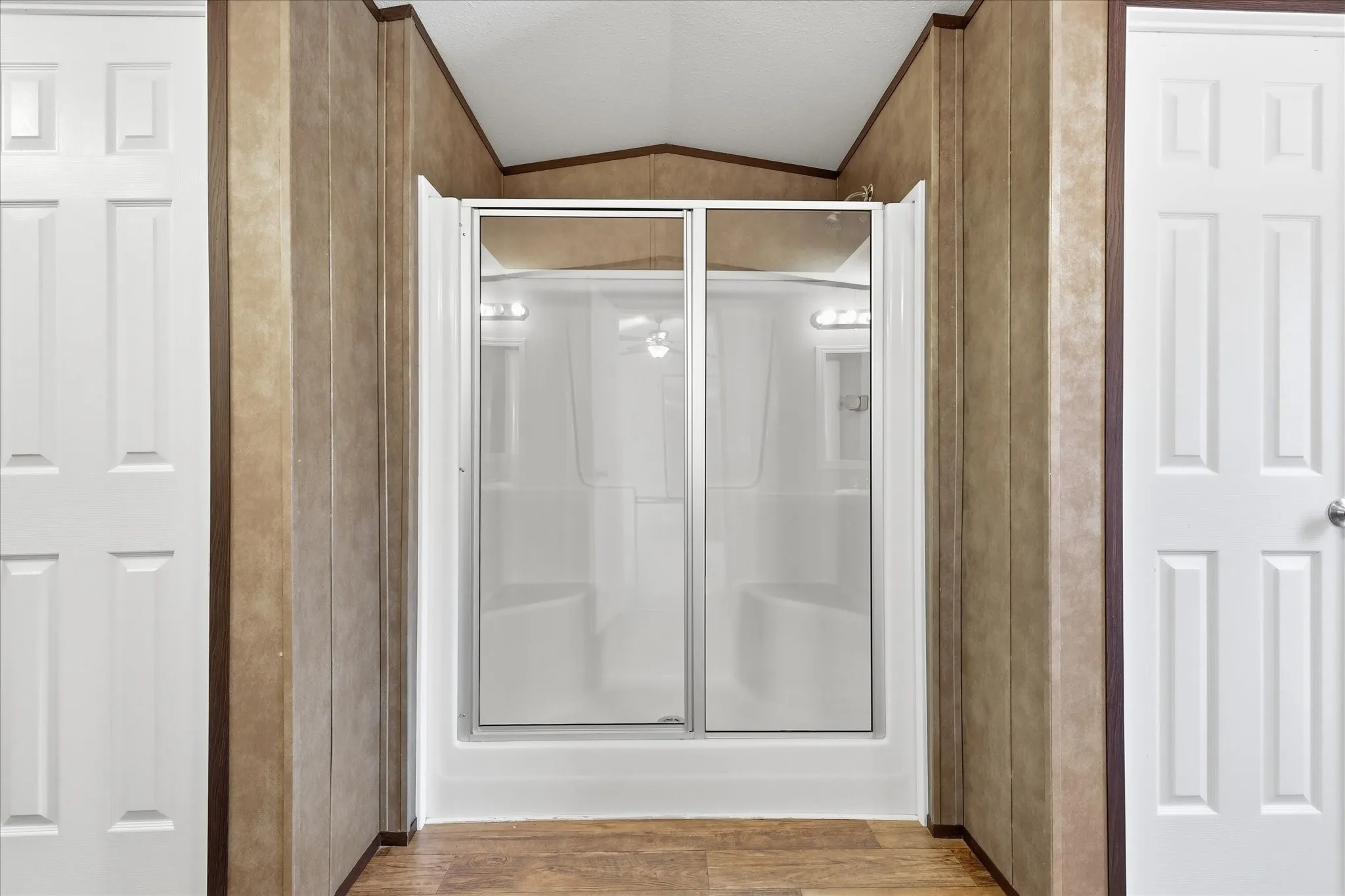 Shower enclosure with sliding glass doors, integrated seating, and overhead lighting