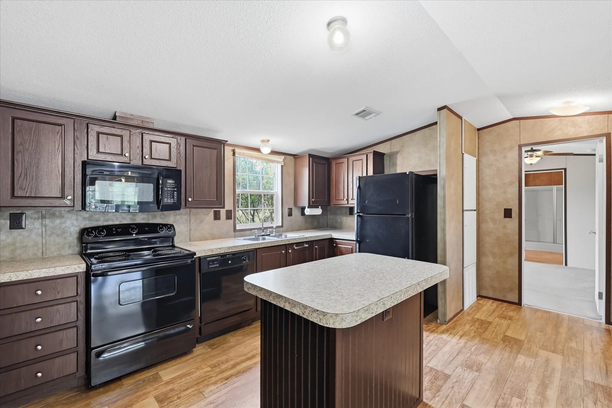 Spacious kitchen featuring rich wood-finish cabinetry, black gas range, black refrigerator, and stainless steel microwave