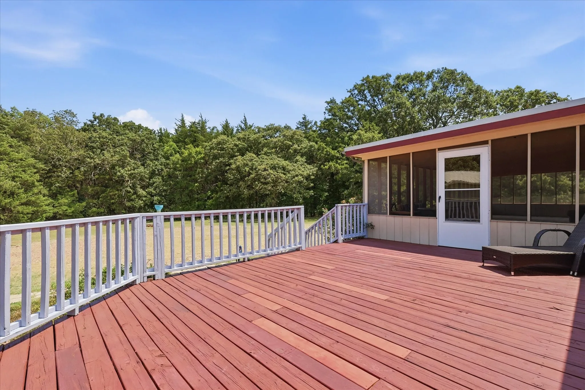 Expansive outdoor deck featuring wood-finish flooring, white railing, and a screened porch with a white exterior door