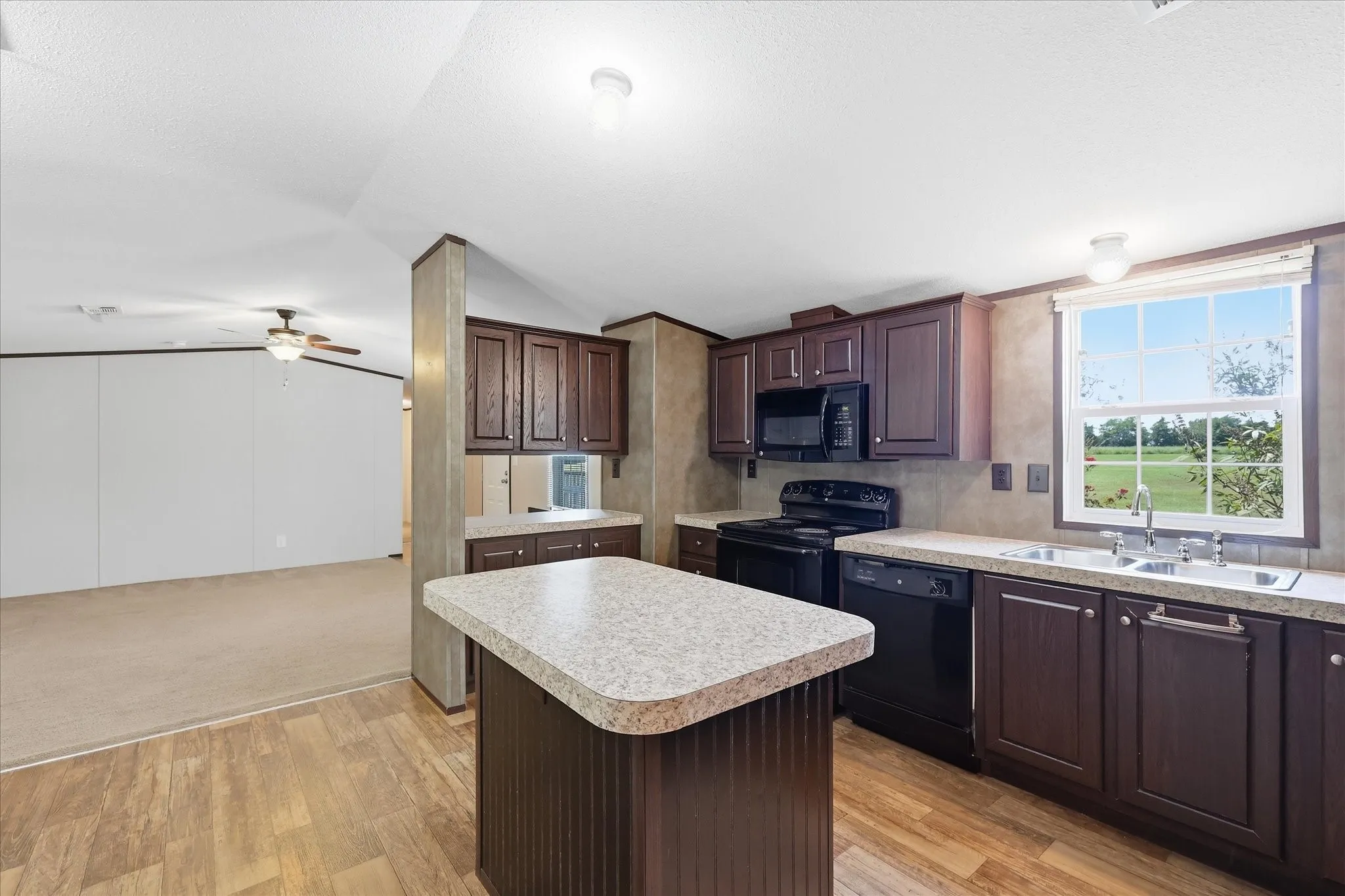 Kitchen featuring an island with a breakfast bar, dark wood-finish cabinetry, black appliances, and light countertops