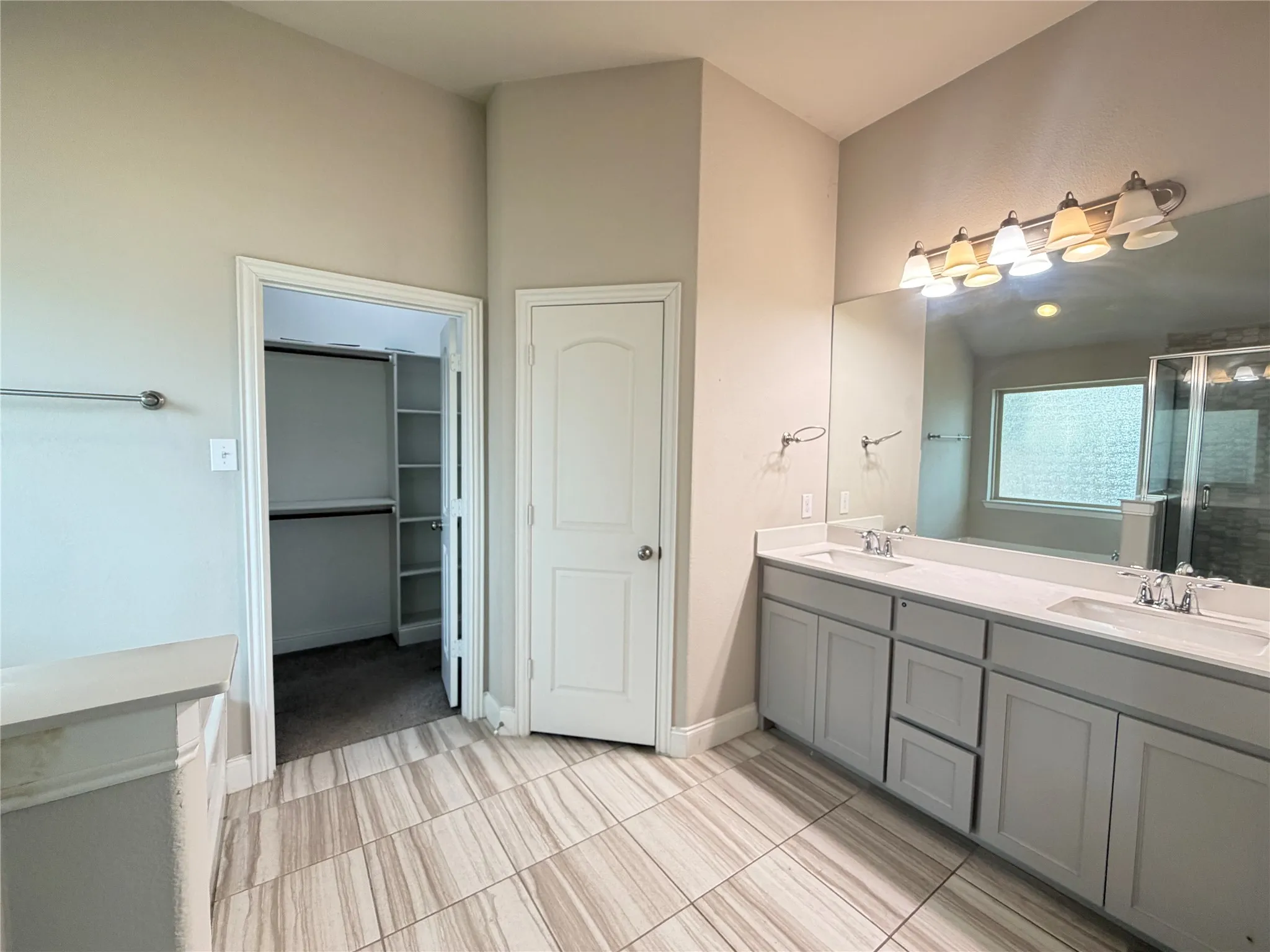 Bathroom featuring wood-look tile flooring, a dual vanity with light gray cabinetry and white countertops, a large mirror, and a window with frosted glass