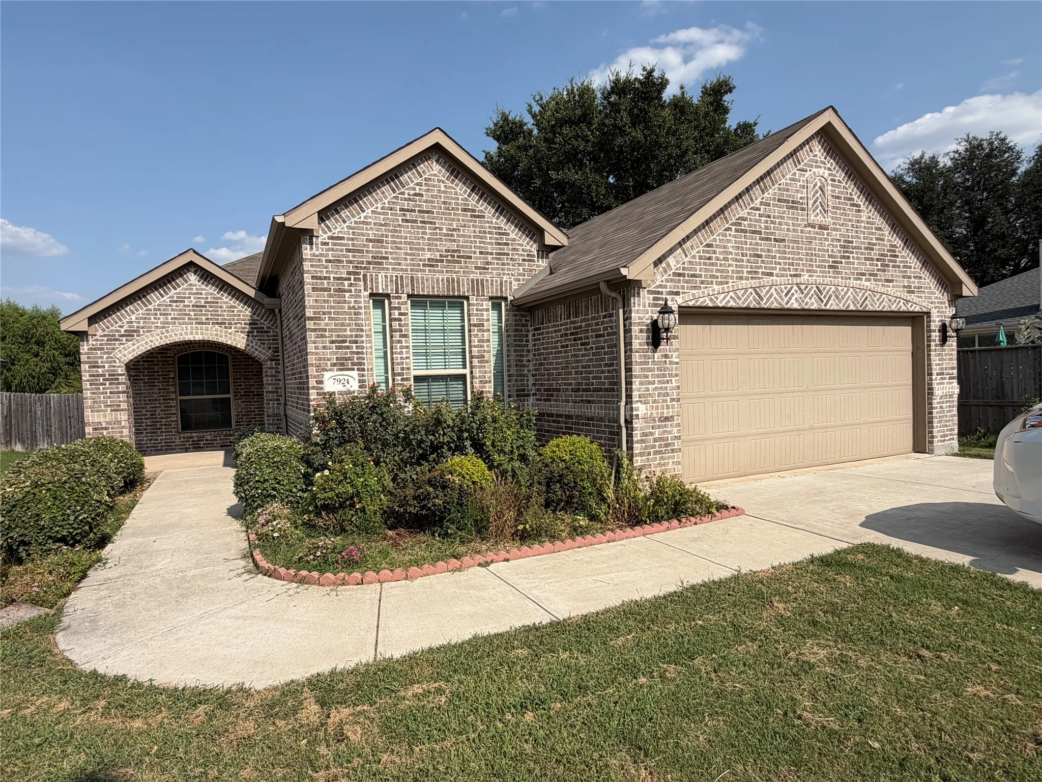 Brick exterior with an arched entry, attached two-car garage, and established landscaping