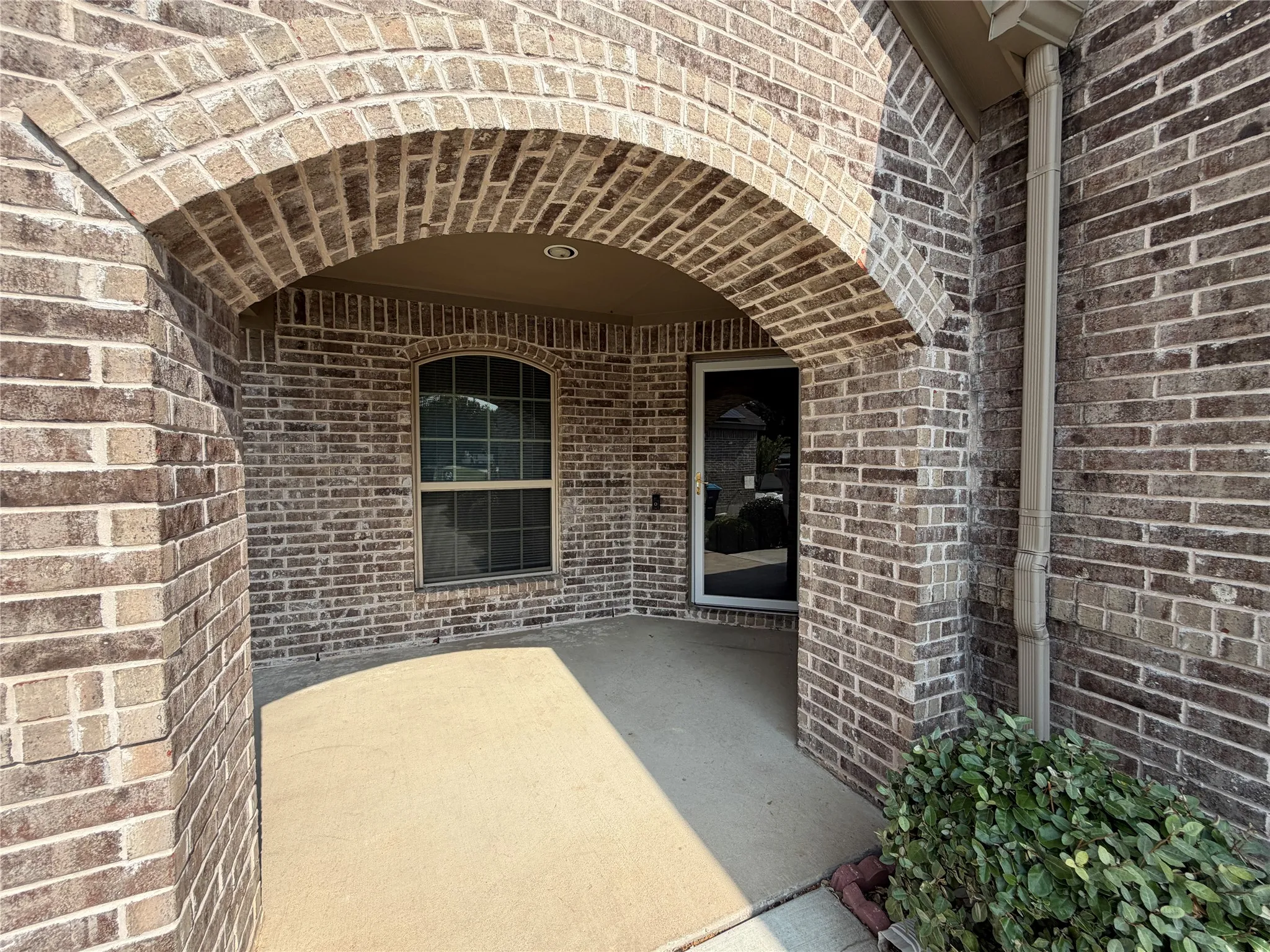 Brick exterior entry featuring an arched portico, concrete porch, and a window with an arched top