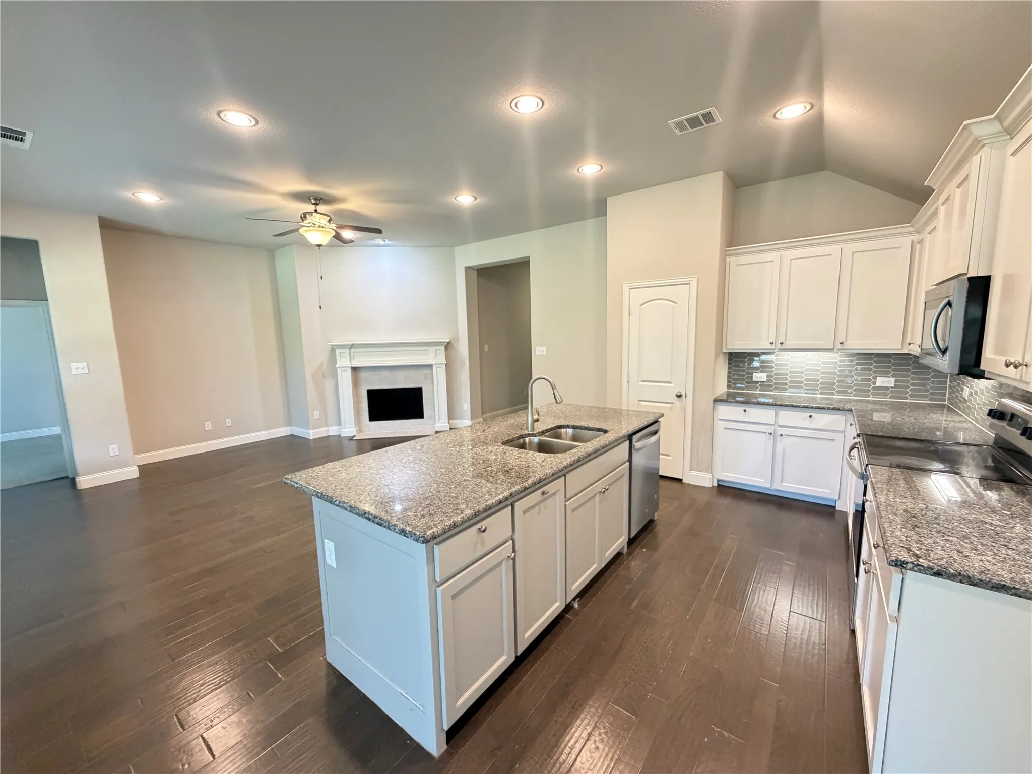 Spacious kitchen featuring an island with a dual-basin sink, granite countertops, white cabinetry, and a subway tile backsplash