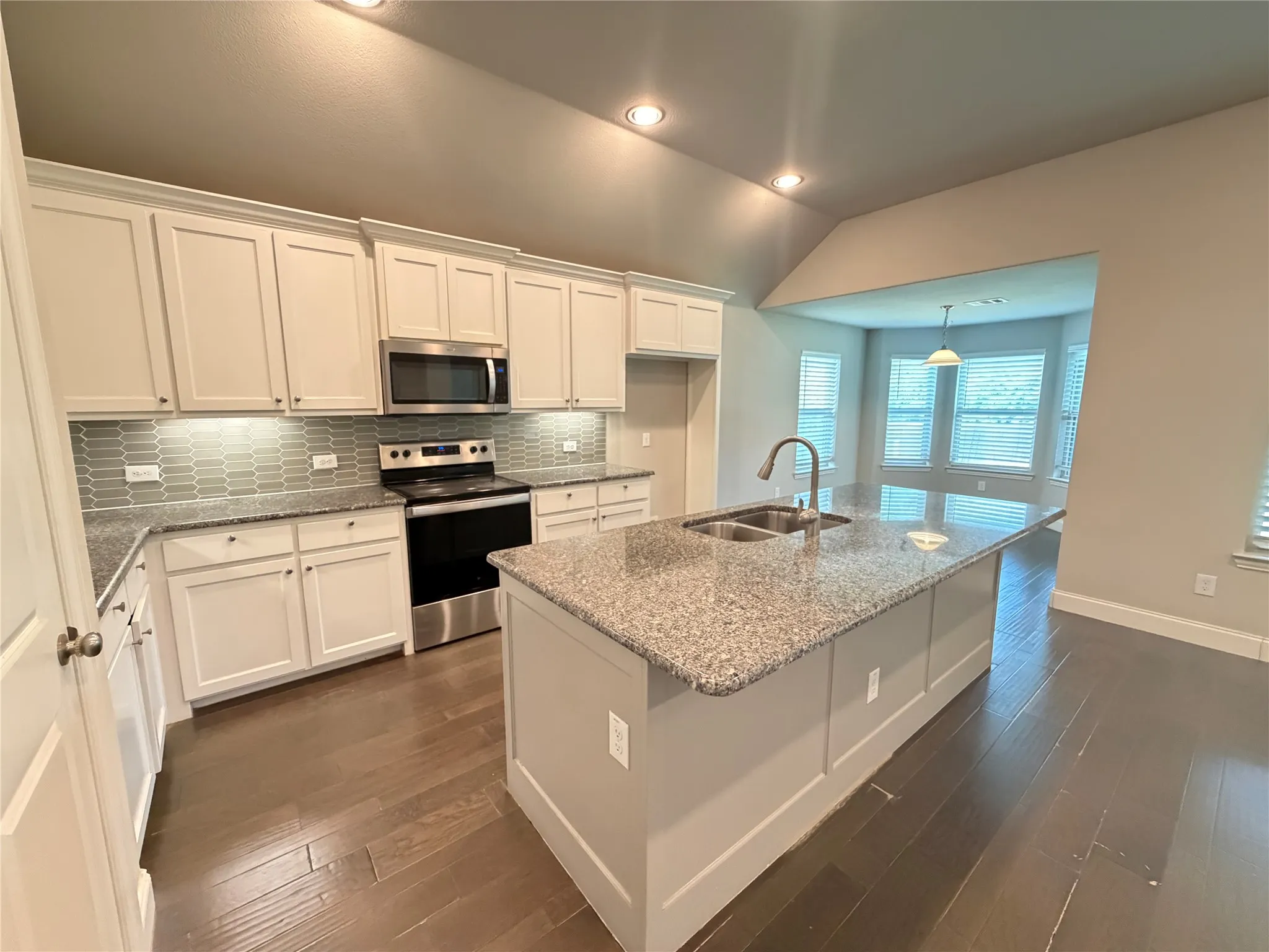 Modern kitchen featuring a central island with a double basin sink, granite countertops, white shaker cabinetry, stainless steel appliances, and wood-finish flooring