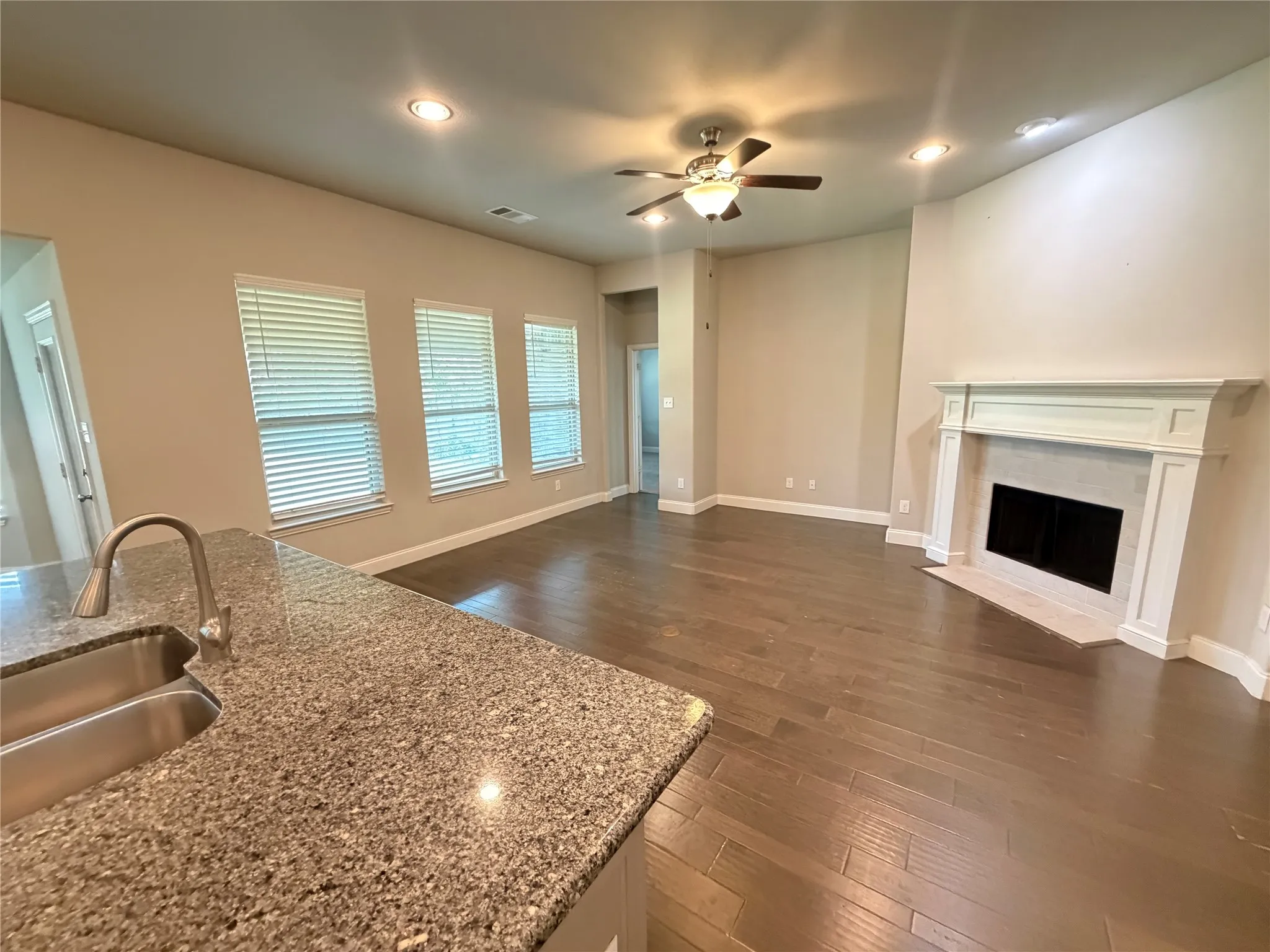 Open-concept living area featuring rich wood-finish flooring, a contemporary fireplace with a decorative mantel, and recessed lighting
