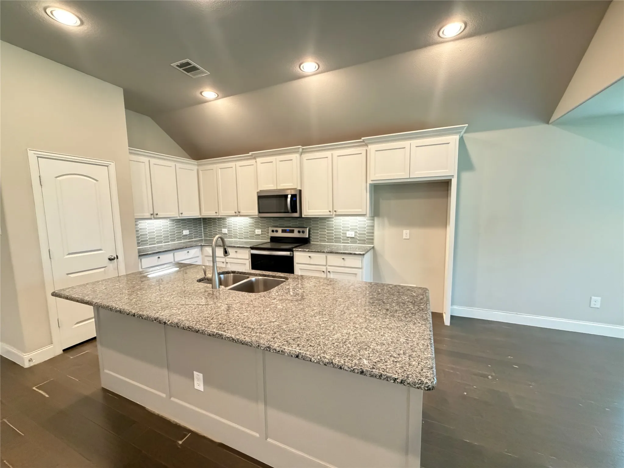 Kitchen featuring a central island with granite countertop and dual basin sink, white cabinetry with under-cabinet lighting, stainless steel appliances, and a tiled backsplash