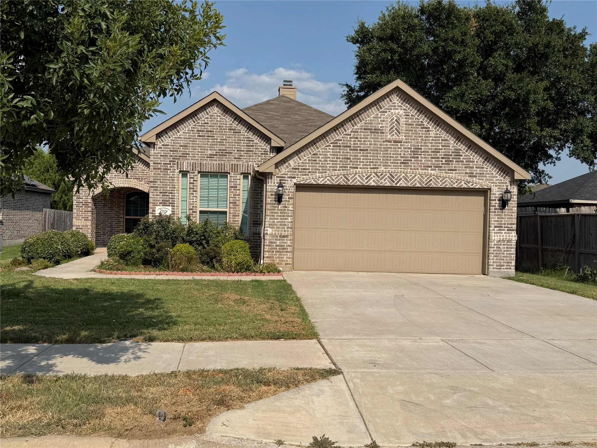 Brick exterior featuring a two-car garage, established landscaping, and a concrete driveway