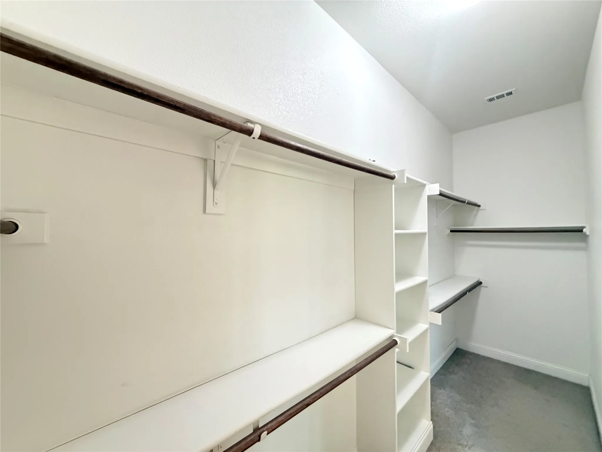 Walk-in closet featuring white walls, multi-level shelving, and multiple clothing rods