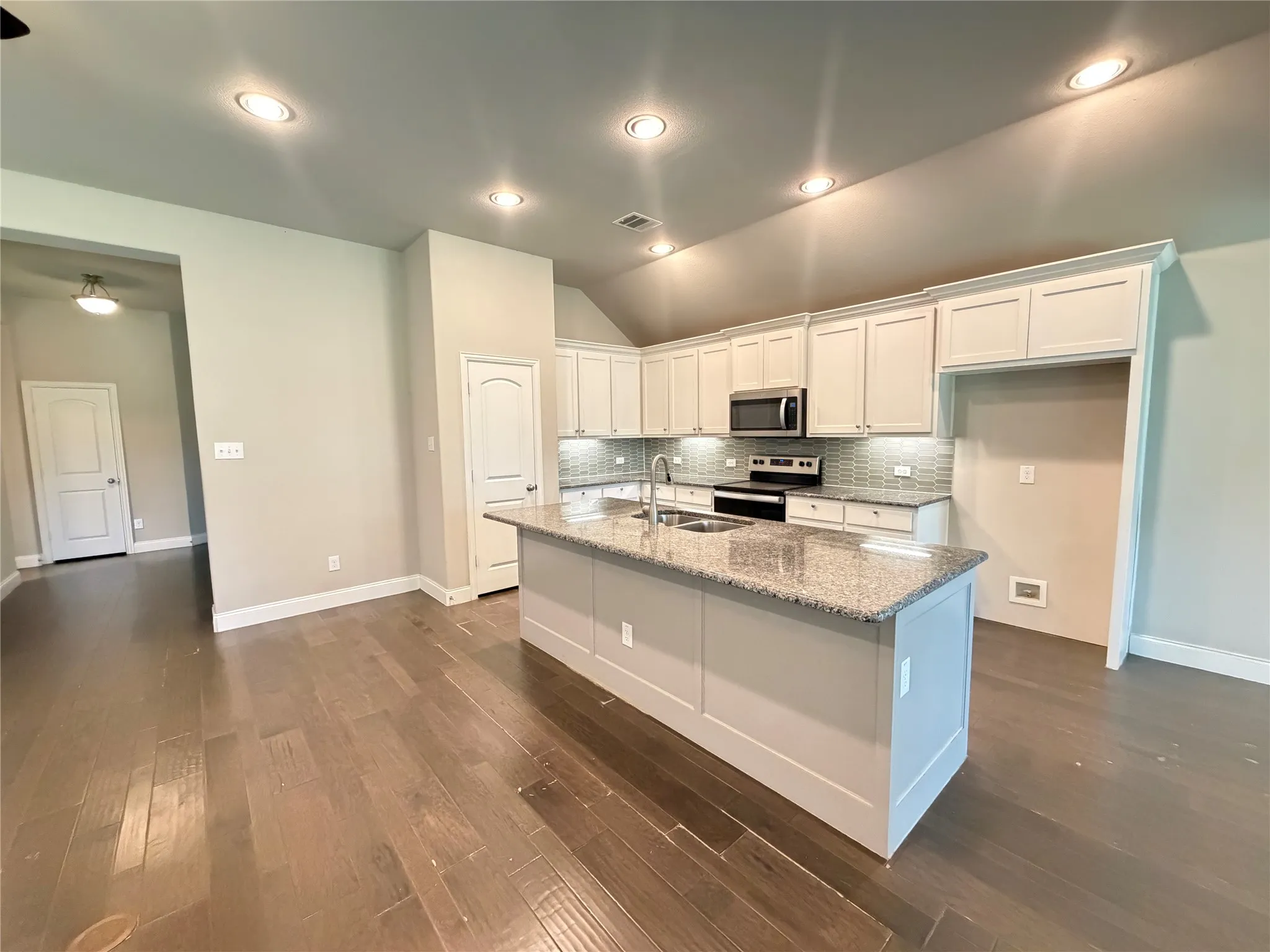 Open-concept kitchen featuring an oversized island with a granite countertop, white shaker cabinetry, stainless steel appliances, and wood-finish flooring