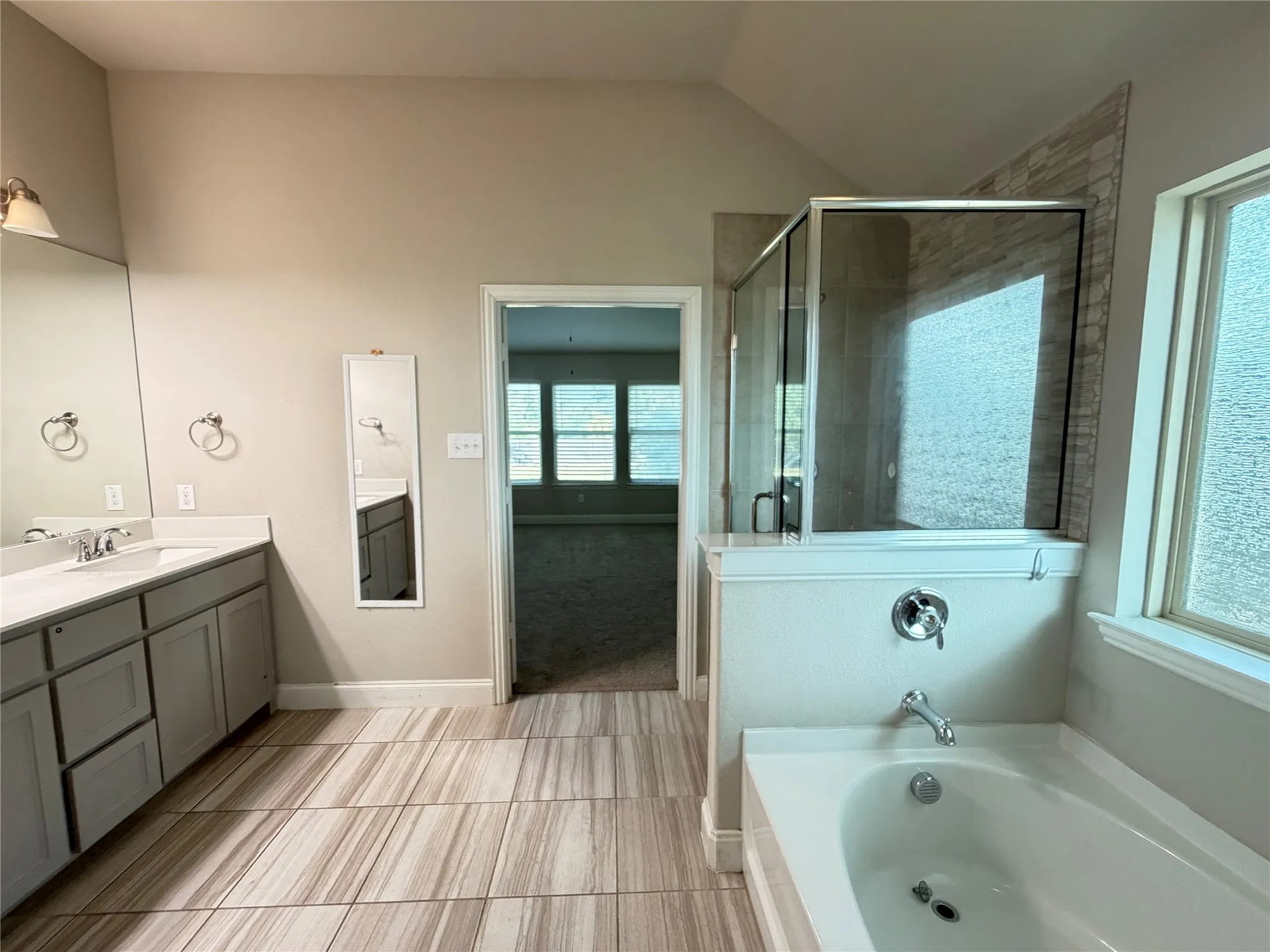 Bathroom featuring a spacious soaking tub, glass-enclosed shower with tile surround, and a dual-sink vanity with white countertop