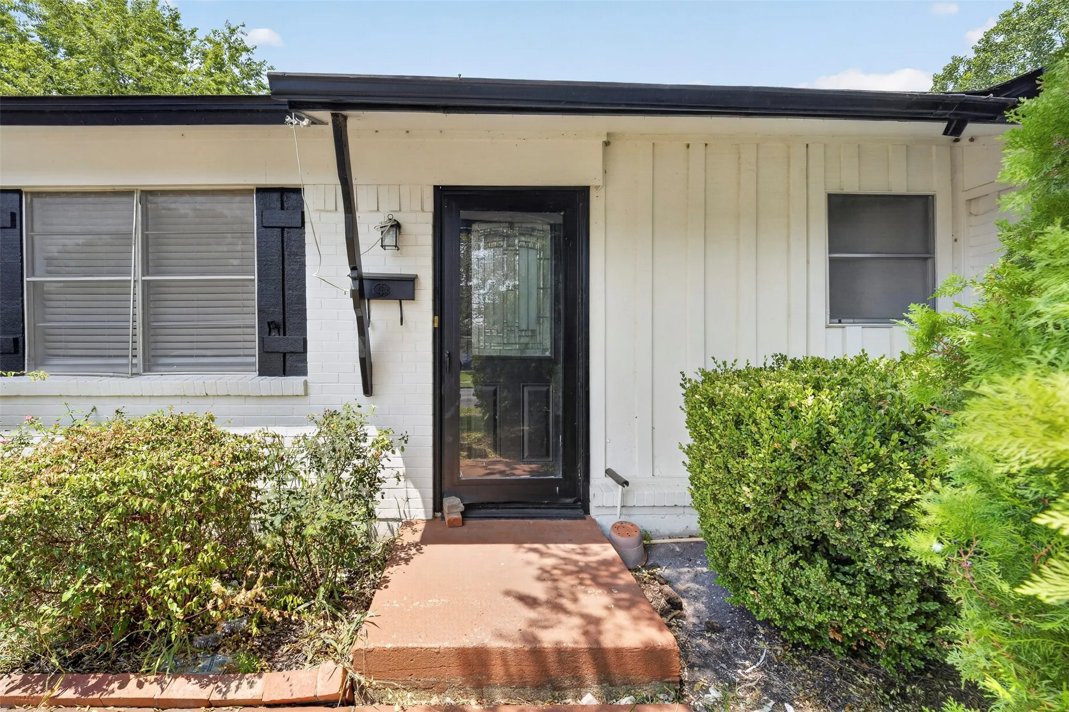Front exterior featuring a dark-framed entry door with decorative glass, brick veneer siding, and board-and-batten siding