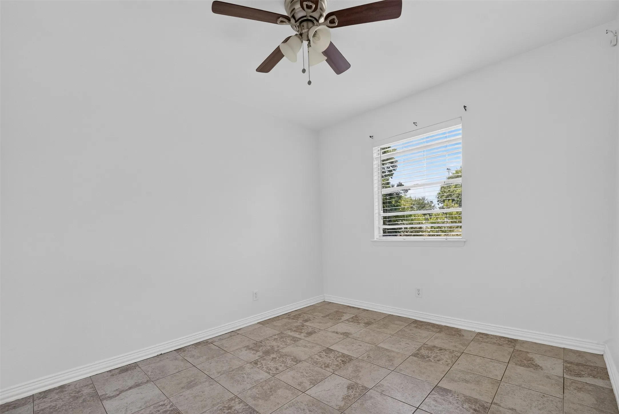 Room featuring neutral-toned tile flooring, white walls, and a ceiling fan with a light kit