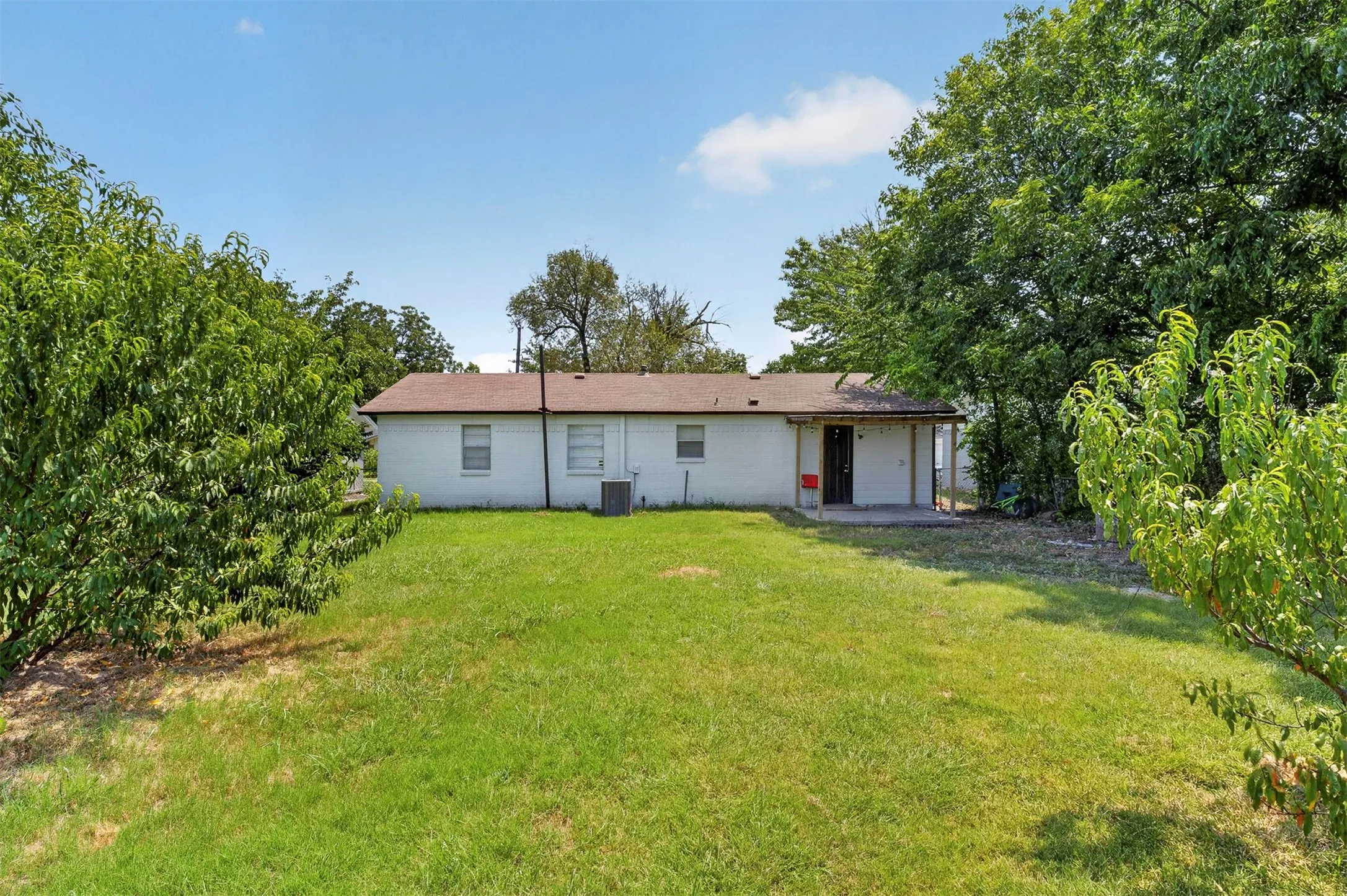 Expansive backyard featuring a lush green lawn, mature trees, and a rear covered patio