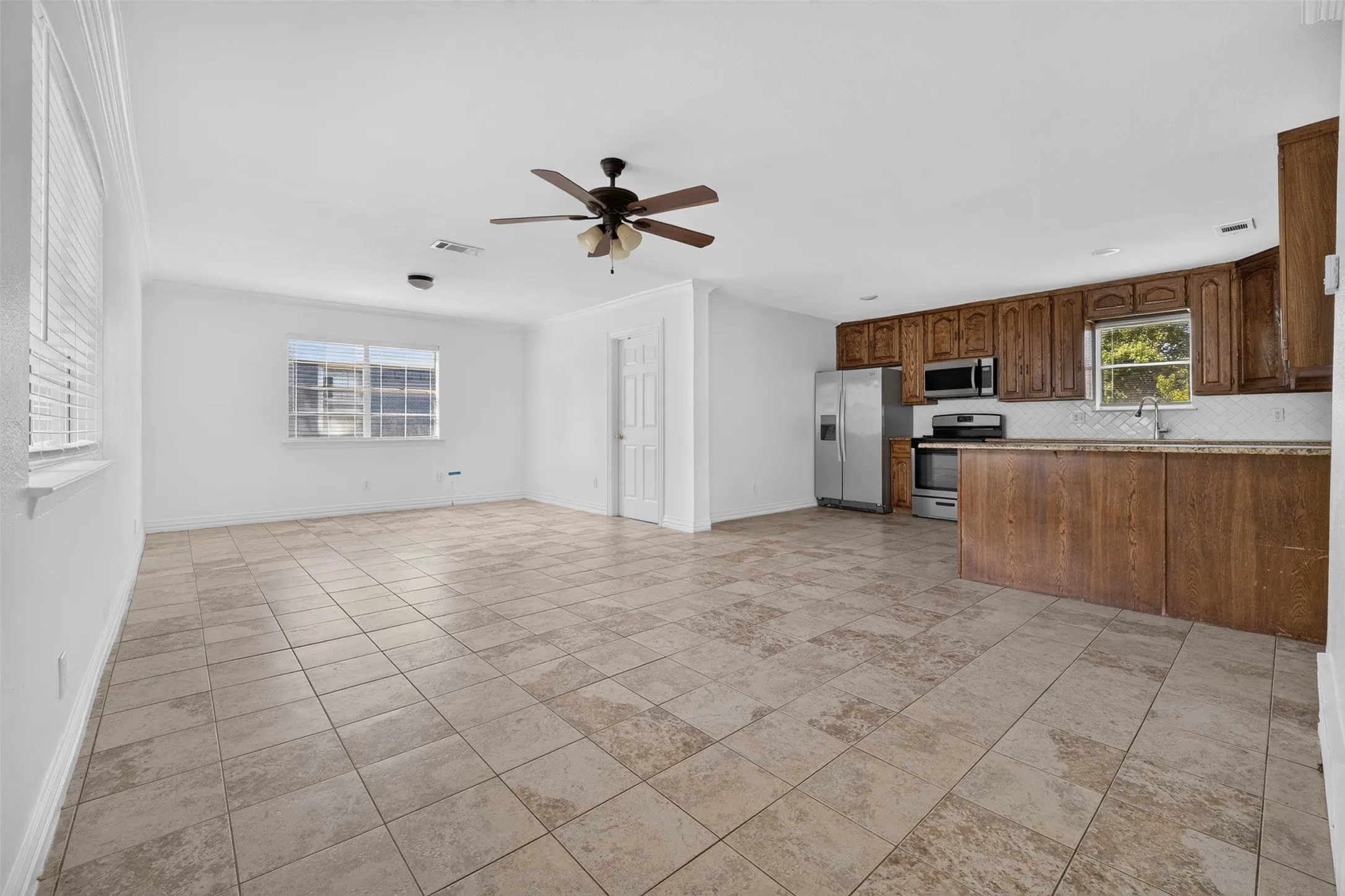 Spacious open-concept room featuring neutral tile flooring, white walls, and a ceiling fan with integrated lighting