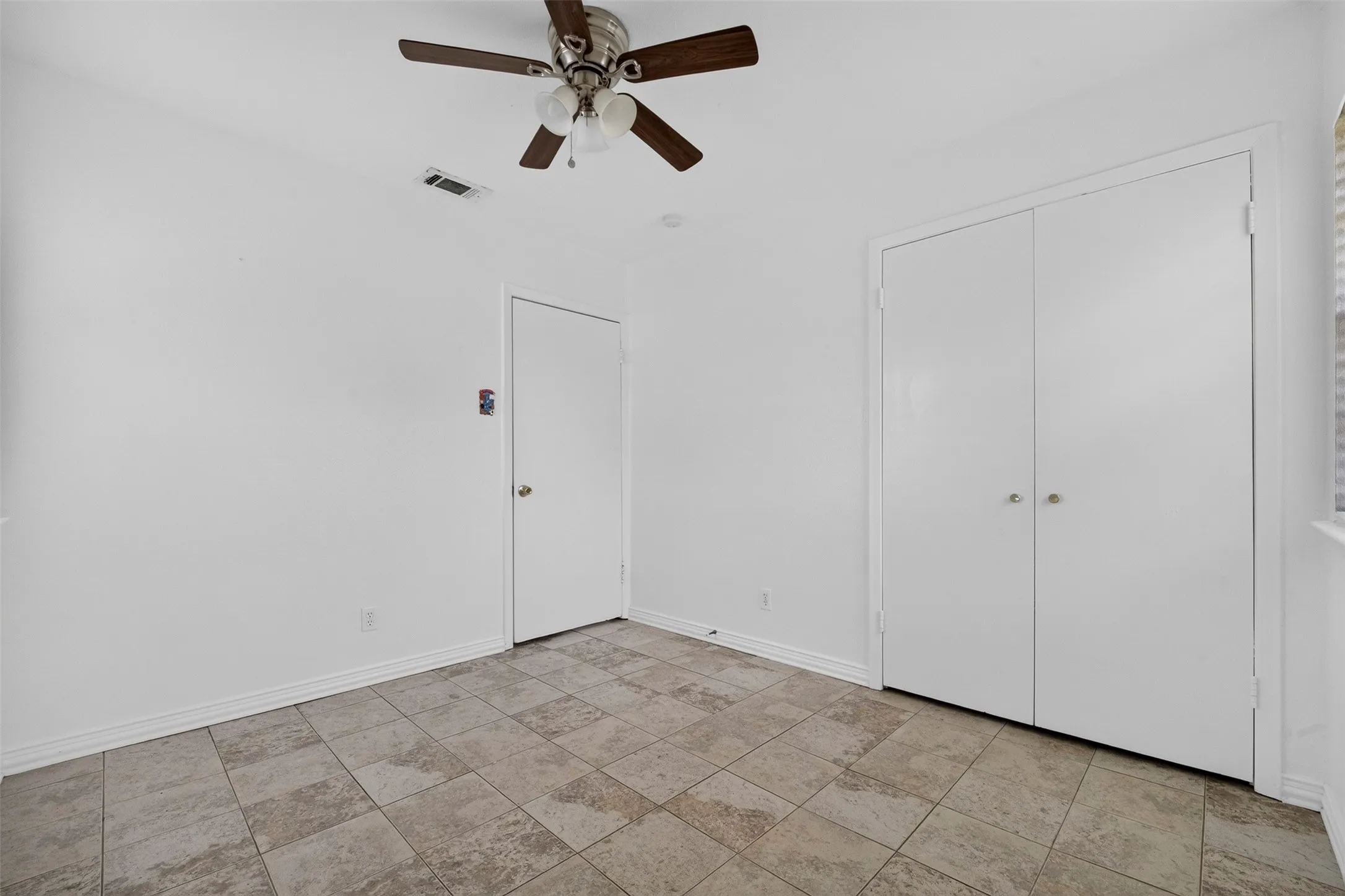 Room featuring a ceiling fan with integrated lighting, tile flooring, and two sets of bi-fold closet doors