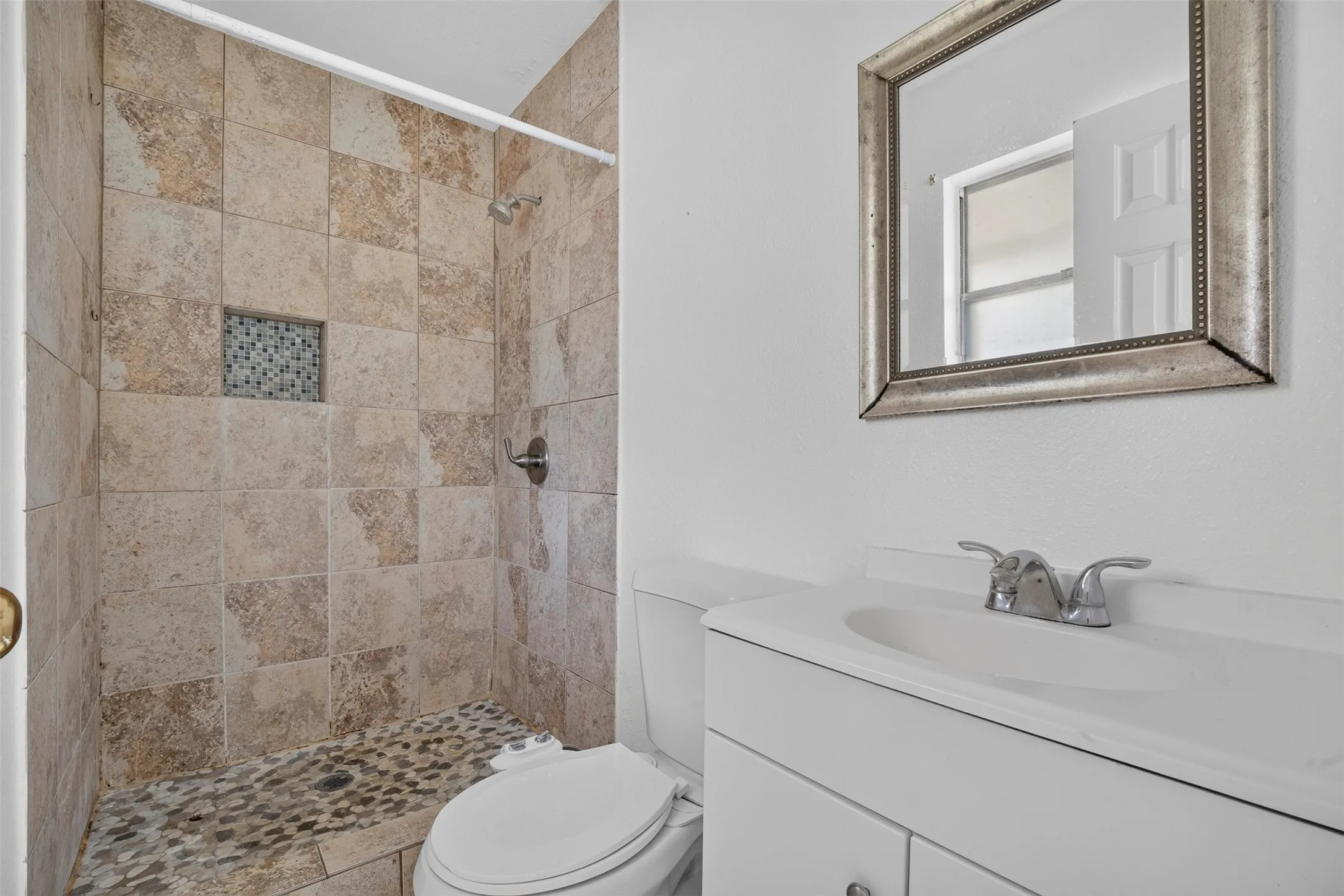 Bathroom featuring a tiled shower with a mosaic niche, pebble flooring in the shower, and a white vanity with an integrated sink