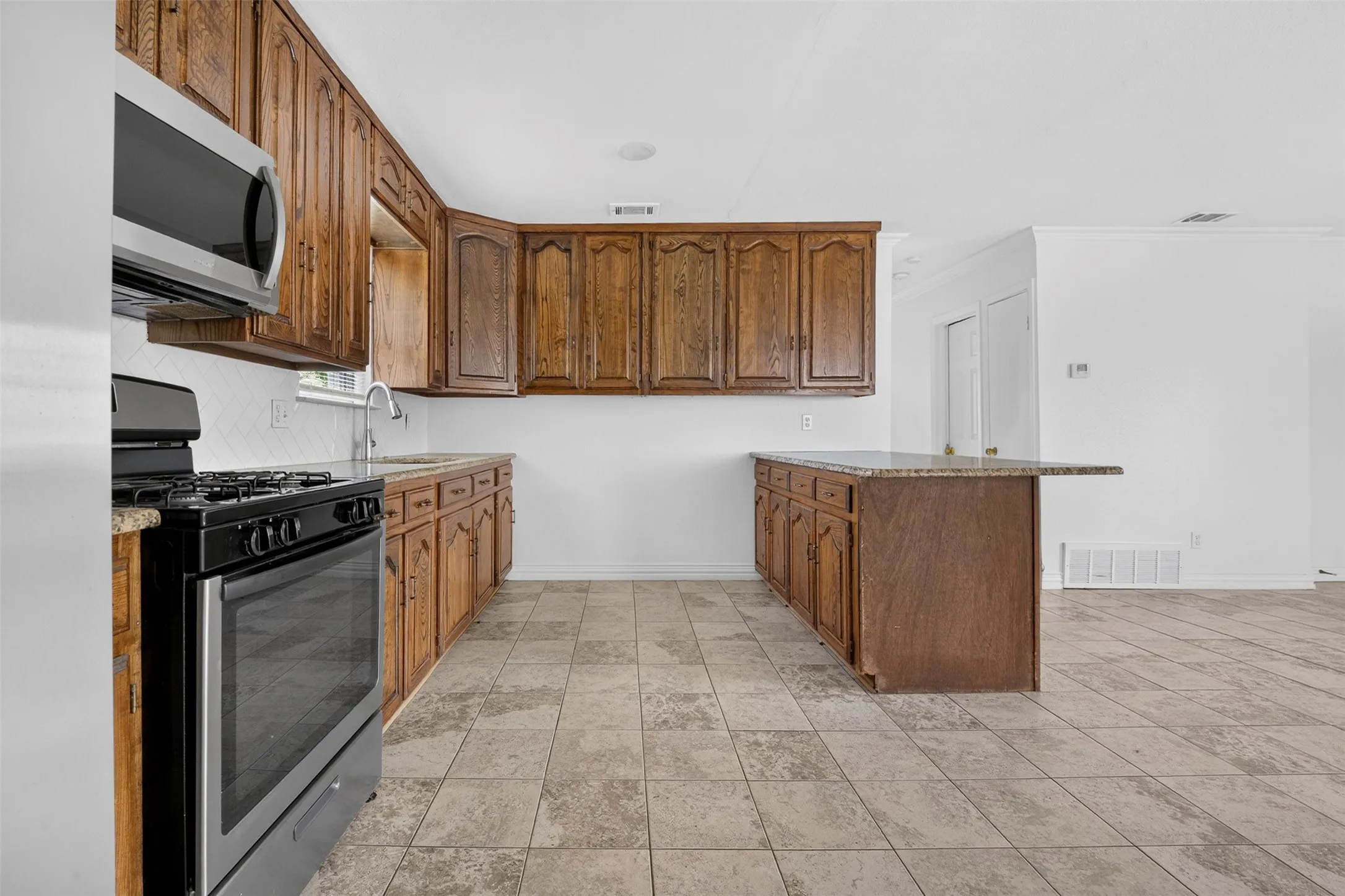 Kitchen featuring rich wood cabinetry, stone countertops, a stainless steel microwave, and a black and stainless steel range