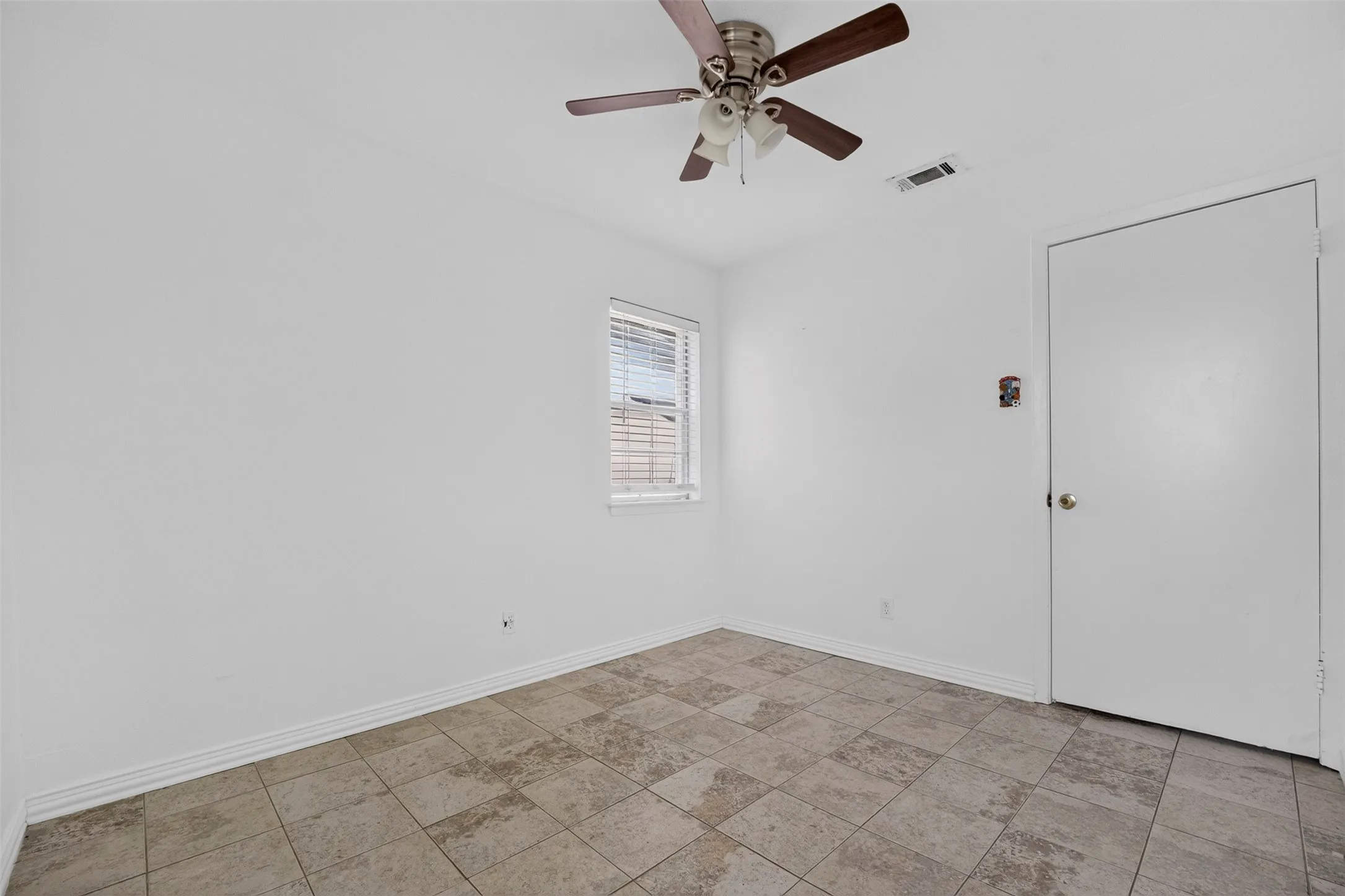 Interior room featuring tiled flooring, a window with blinds, a ceiling fan, and a white interior door