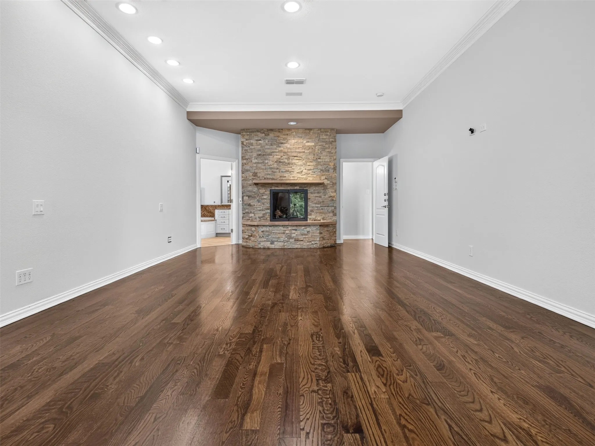 Hardwood flooring, recessed lighting, and a stone fireplace