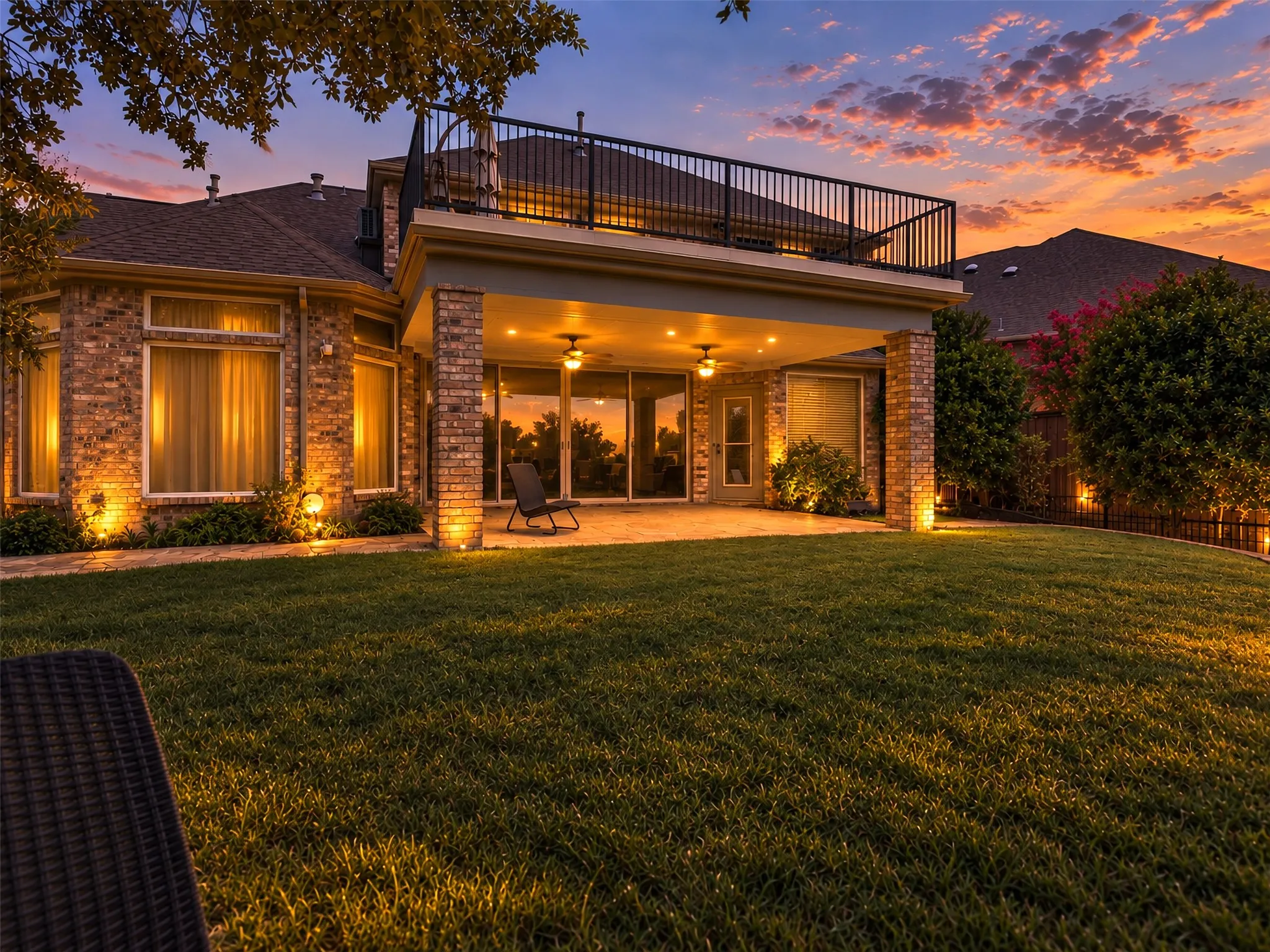 Brick exterior with a covered patio, second-story balcony with metal railing, and a manicured lawn